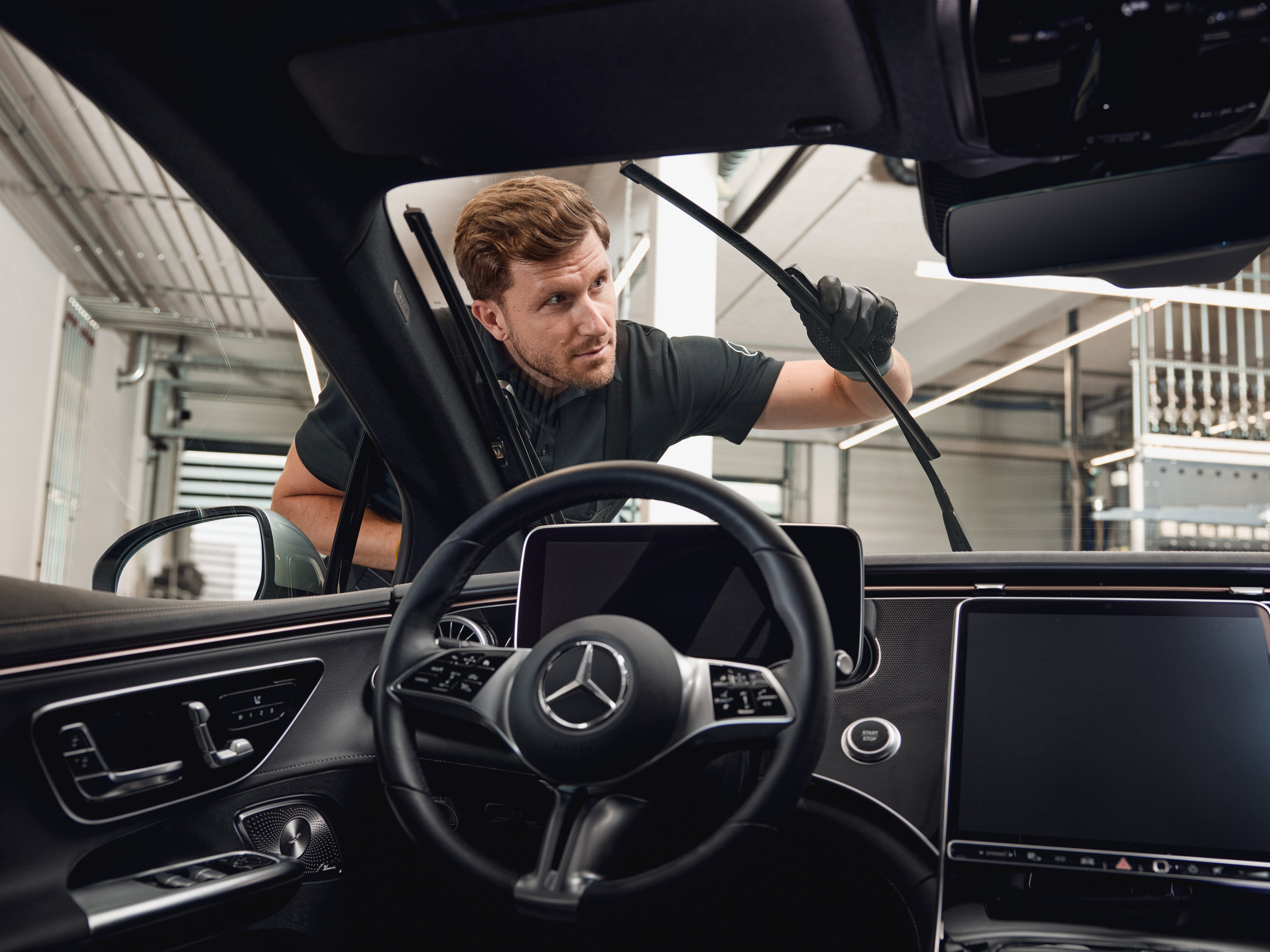 Vue intérieure d'un véhicule Mercedes-Benz avec un technicien remplaçant des balais d'essuie-glace d'origine.