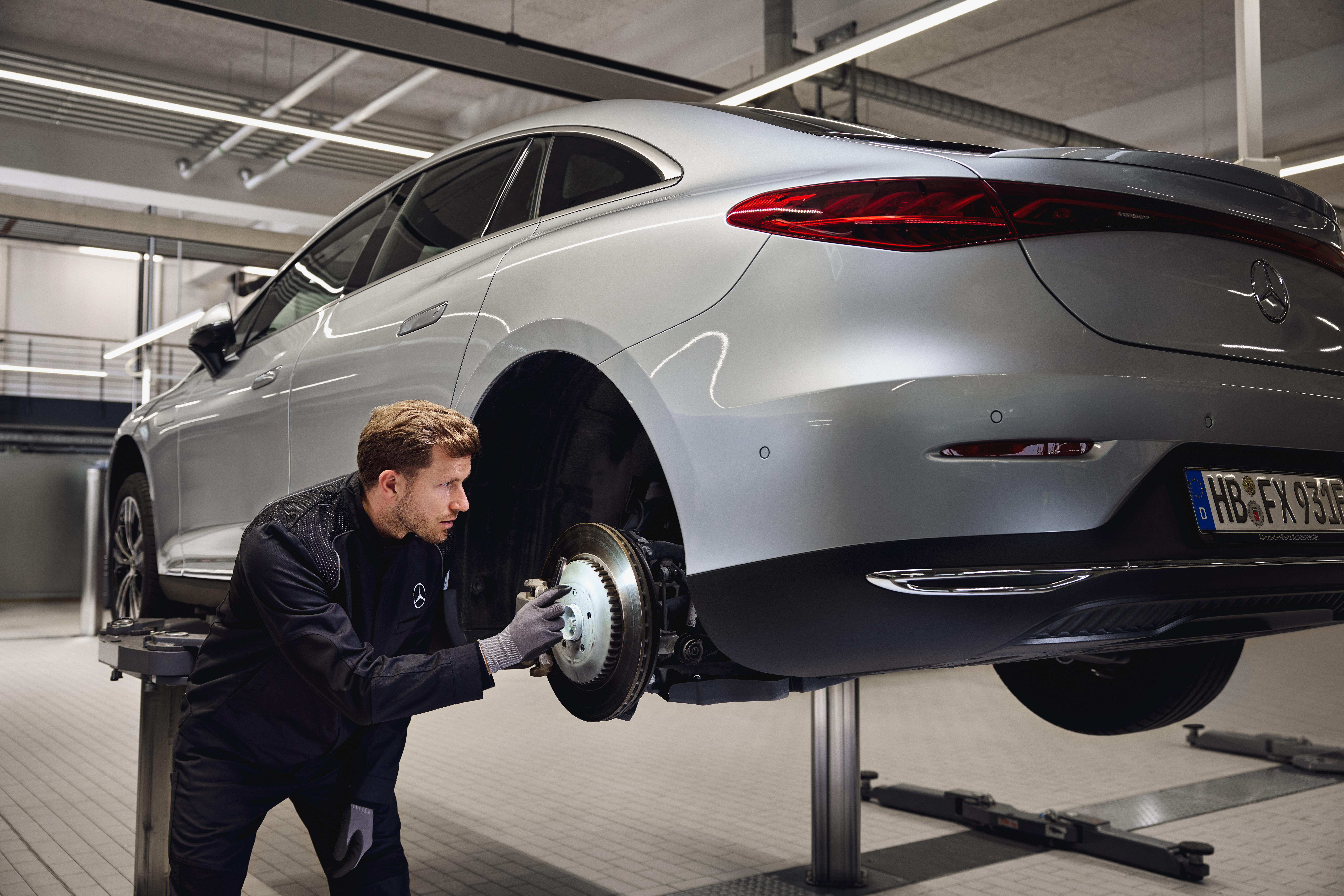 Remplacement des freins d'origine Mercedes-Benz Un véhicule Mercedes-Benz surélevé sur un pont élévateur, avec un technicien en train d'inspecter le système de freinage arrière dans le cadre d'une maintenance avec remplacement de pièces d'origine.