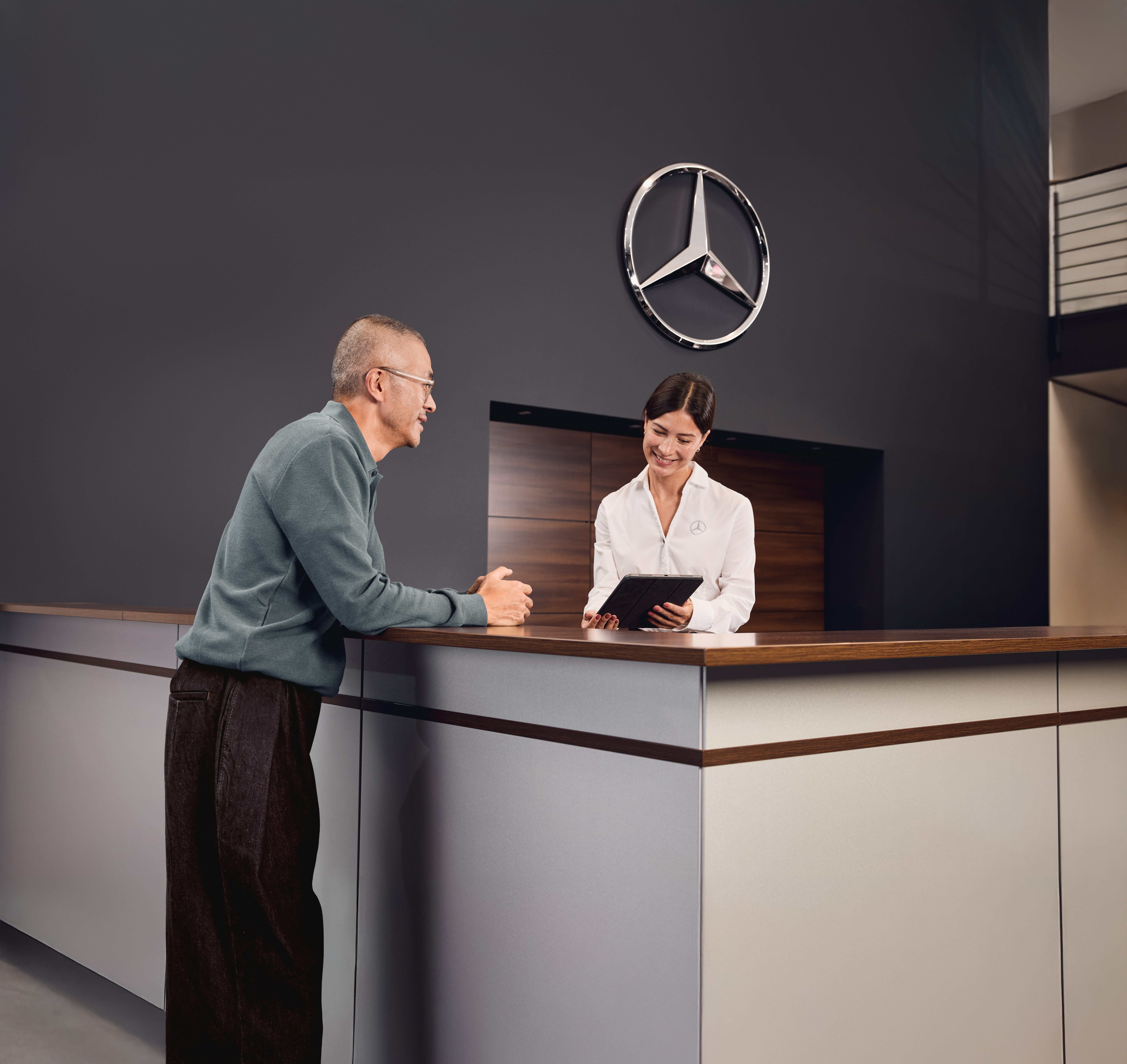 Conseils sur les pièces d'origine Mercedes-Benz Accueil du service après-vente d'un distributeur Mercedes-Benz, où un client discute des détails de la maintenance de son véhicule avec un conseiller du service après-vente.