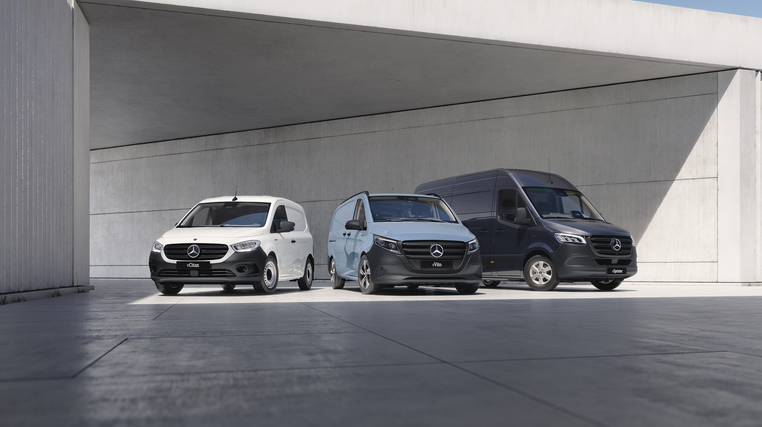 The Mercedes-Benz eSprinter, eCitan and eVito are lined up on display, with the eVito docked at a charging station.