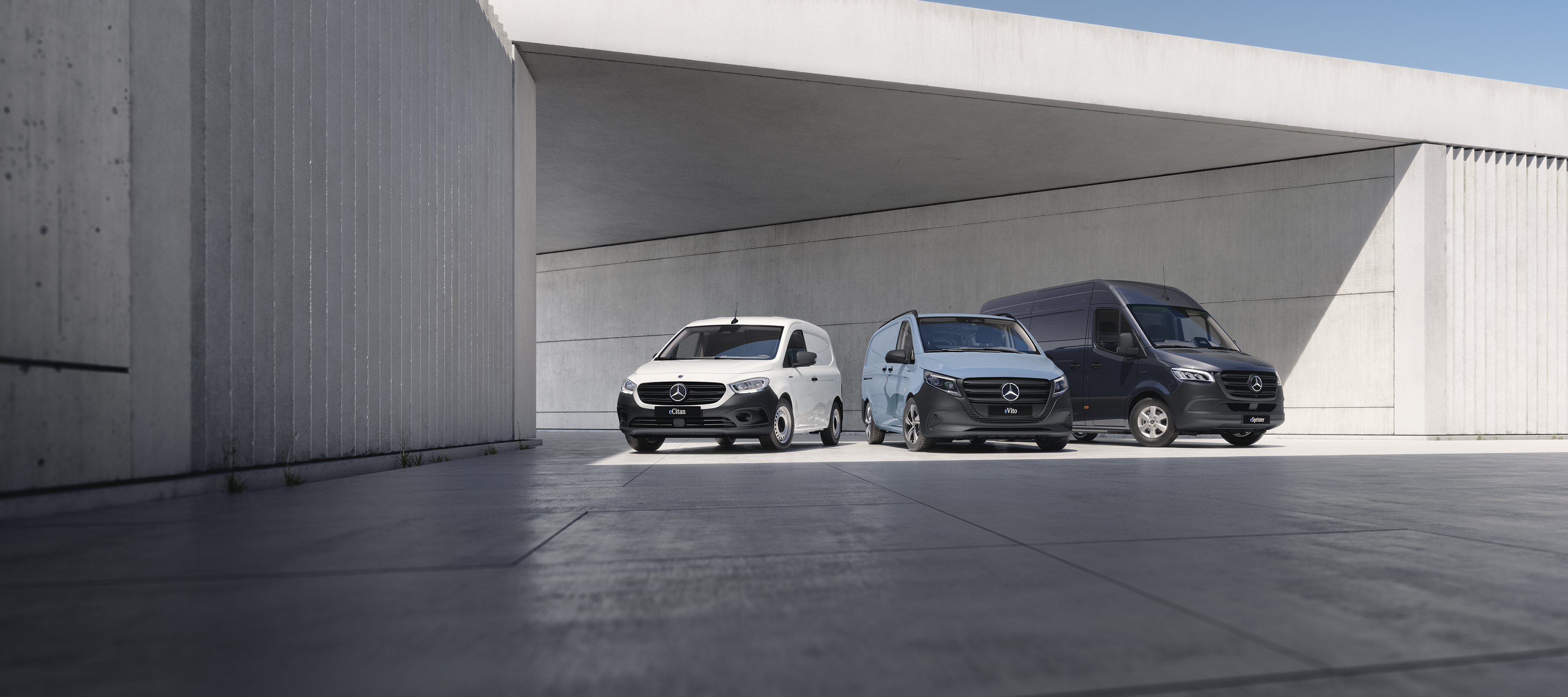 The Mercedes-Benz eSprinter, eCitan and eVito are lined up on display, with the eVito docked at a charging station.