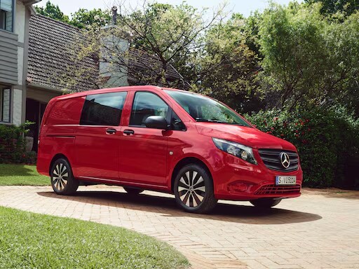 Mercedes-Benz Vito Mixto rouge stationné devant une maison avec jardin.