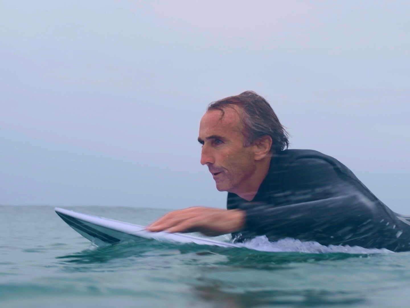 Surfeur allongé sur une planche de surf en mer au lever du jour.