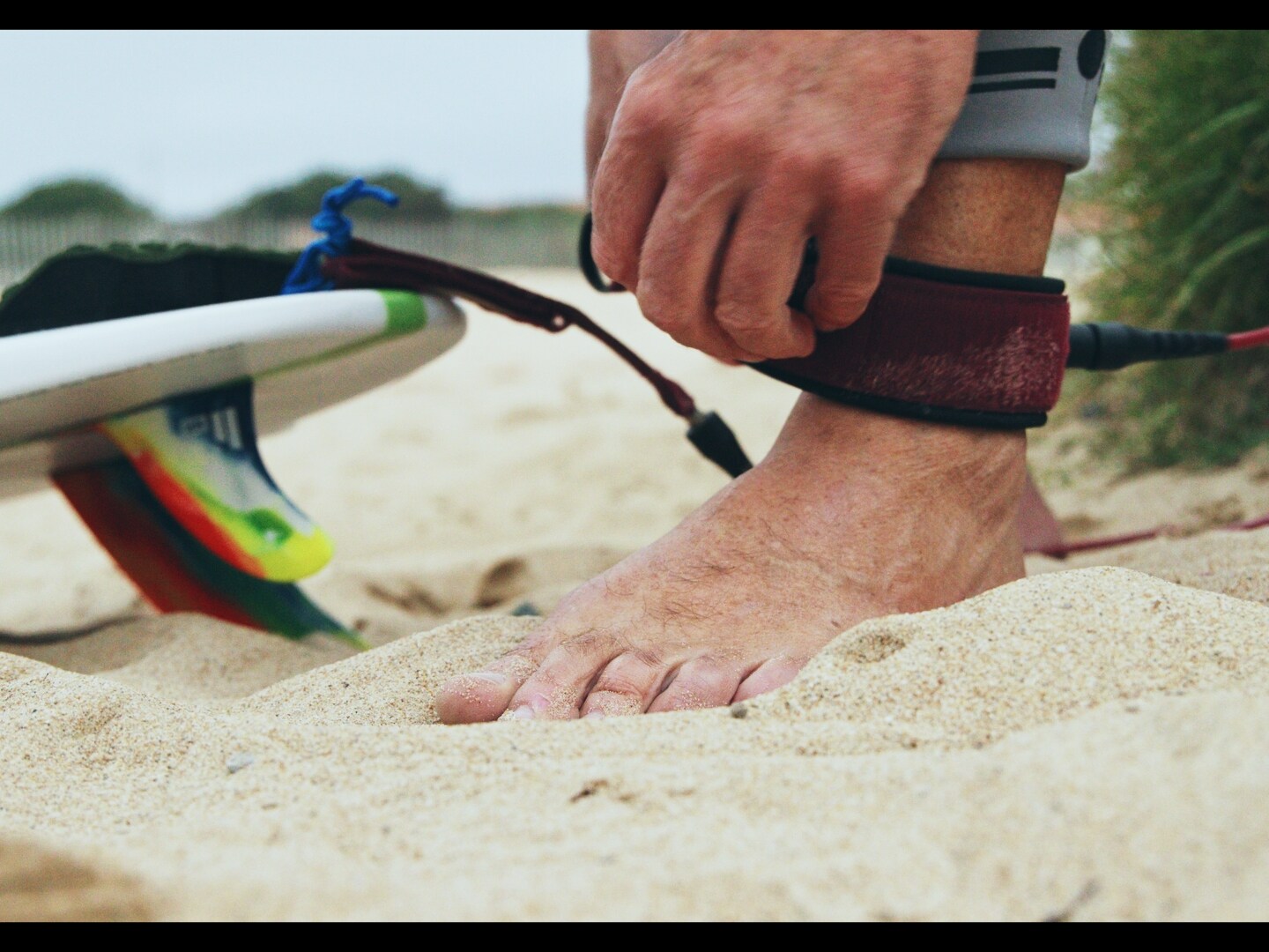Personne attachant le leash de sa planche de surf sur la plage.
