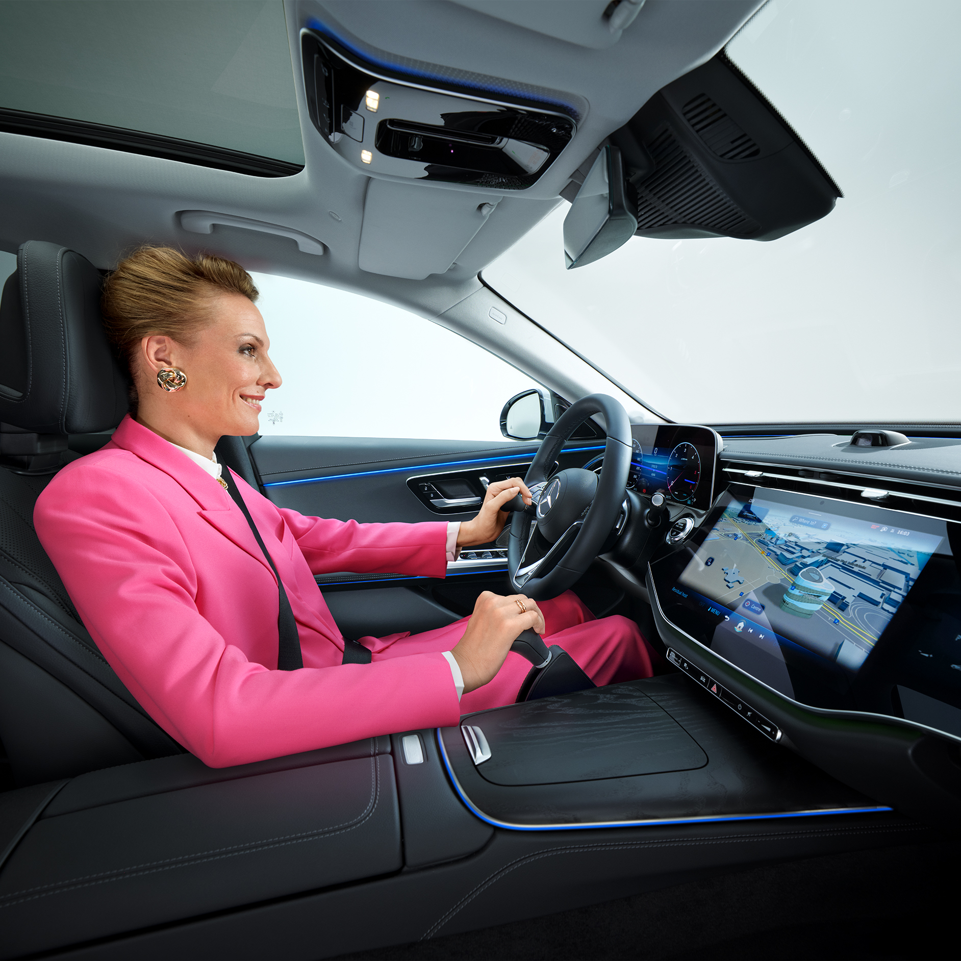 Guide « More Mobility » | Aides à la conduite | Mercedes-Benz Vue intérieure d'une Mercedes-Benz Classe E convertie en voiture accessible, avec une femme au volant utilisant un bouton de volant et une unité de commande manuelle.