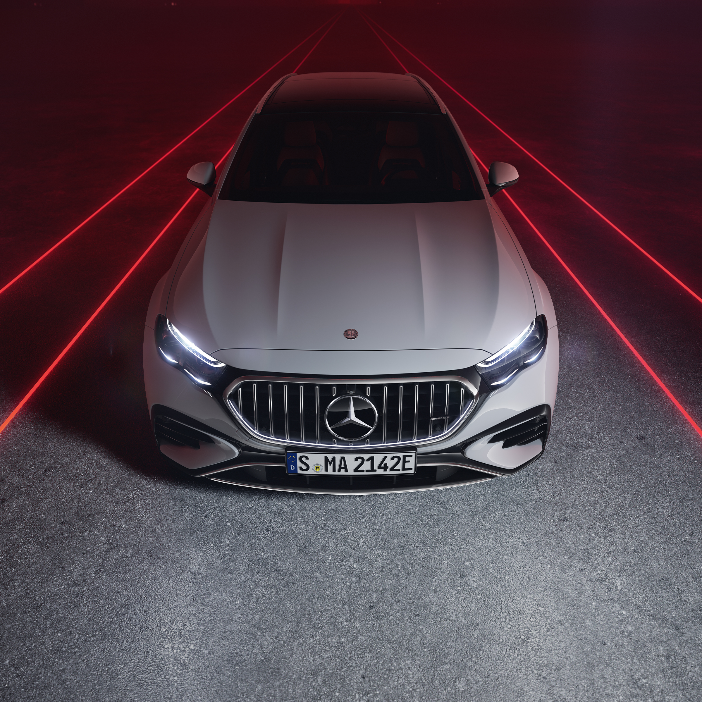 Mercedes-AMG E 53 HYBRID 4MATIC+ de face sur fond rouge, vue de dessus.
