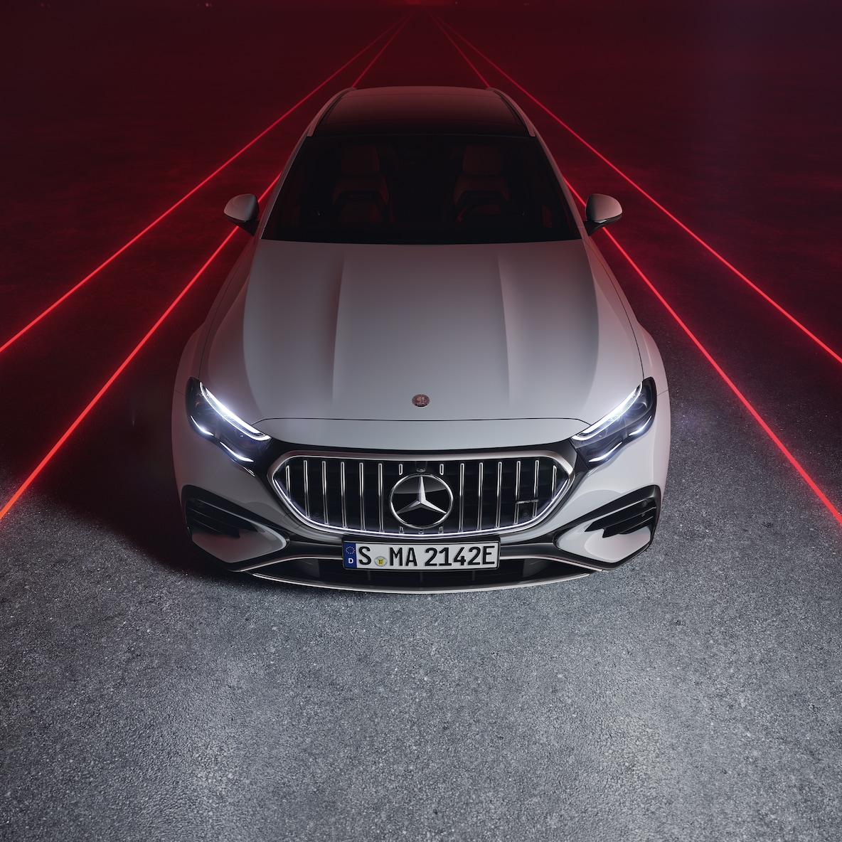 Mercedes-AMG E 53 HYBRID 4MATIC+ de face sur fond rouge, vue de dessus.