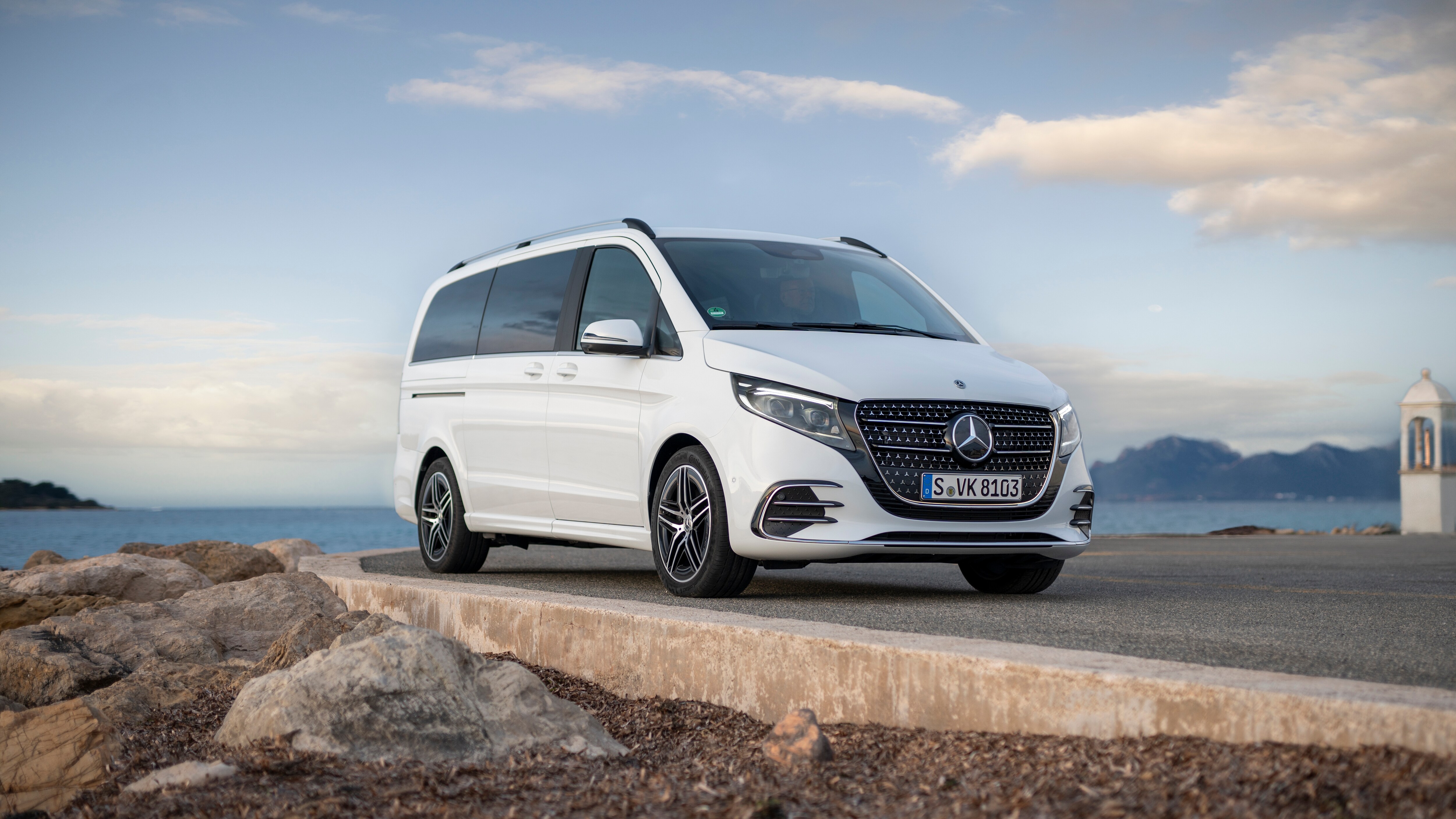Mercedes-Benz Classe V blanche stationnée en bord de mer sur une route côtière.