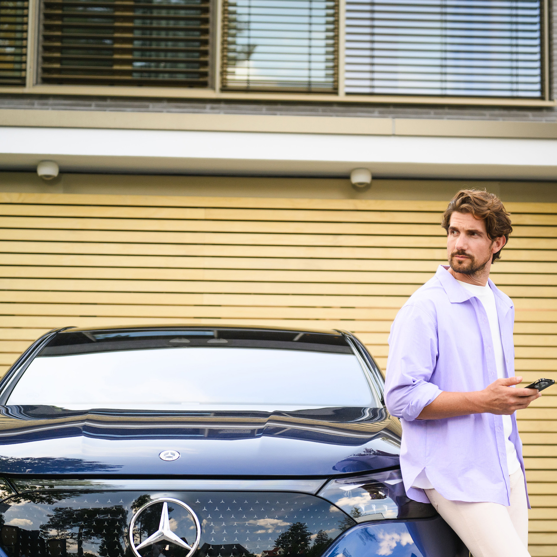 Fleet Personne tenant un smartphone à côté d'une Mercedes-Benz stationnée devant un bâtiment moderne.