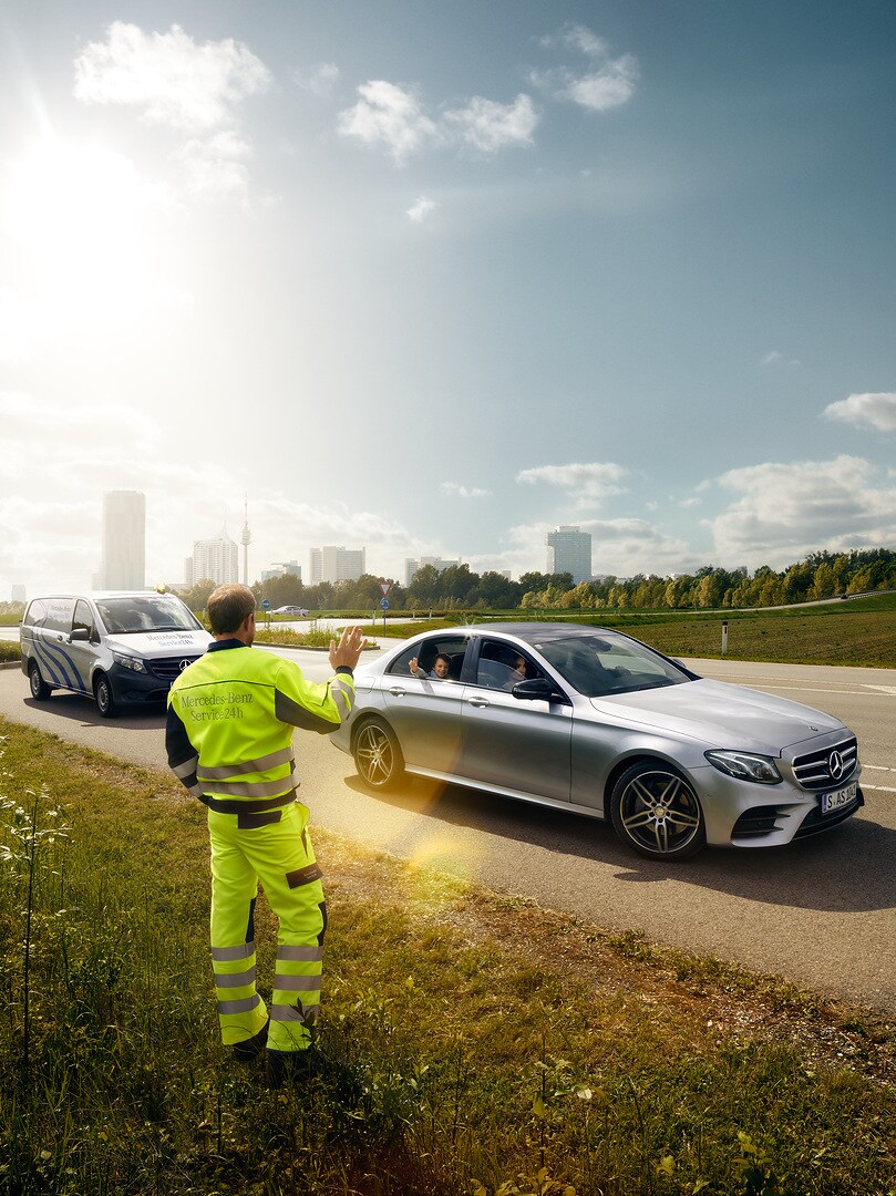 Depuis le bord de la route, un technicien de maintenance Mercedes-Benz fait signe à un enfant assis dans une Mercedes qui démarre.