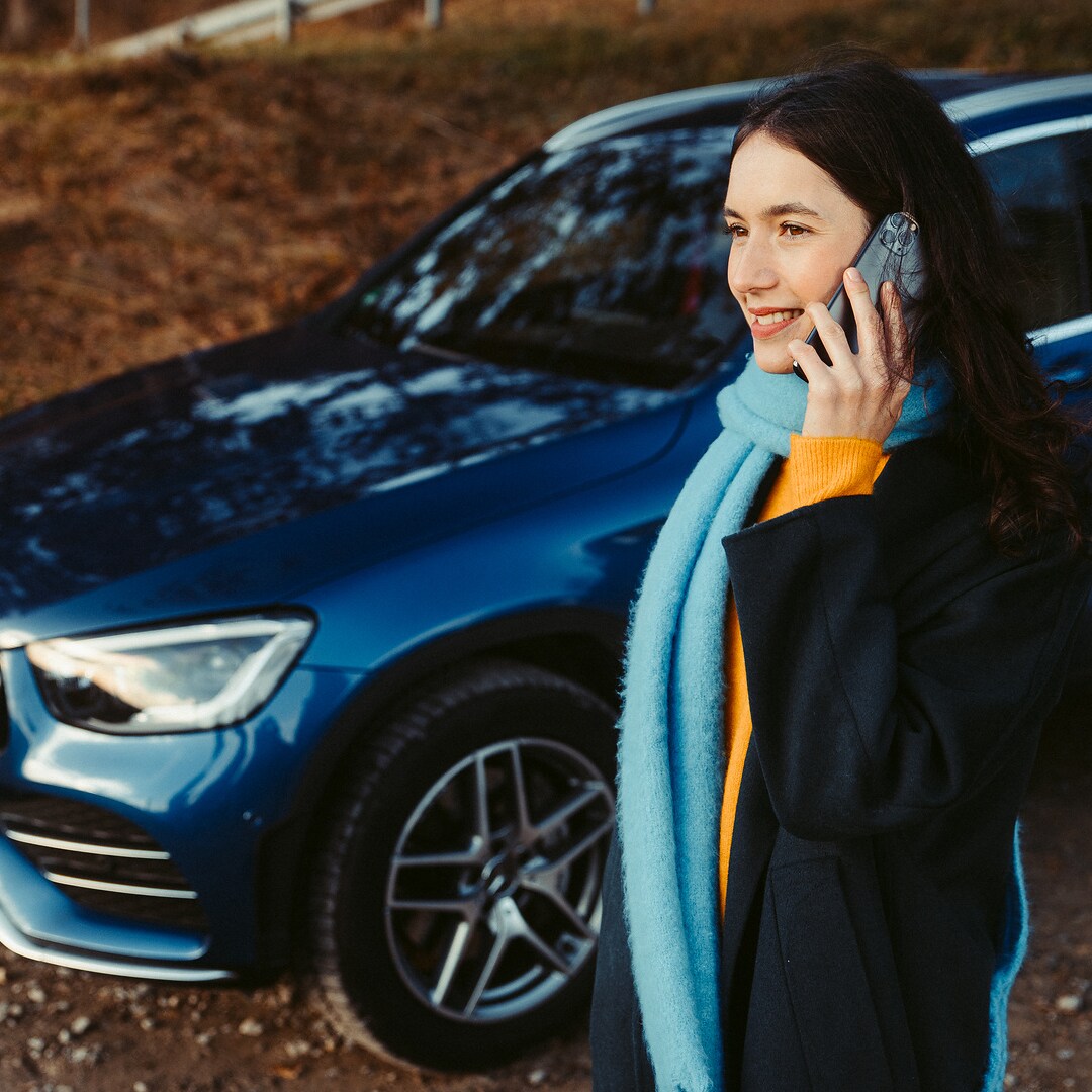 Une femme se tient devant son SUV Mercedes et parle au téléphone avec un smartphone.