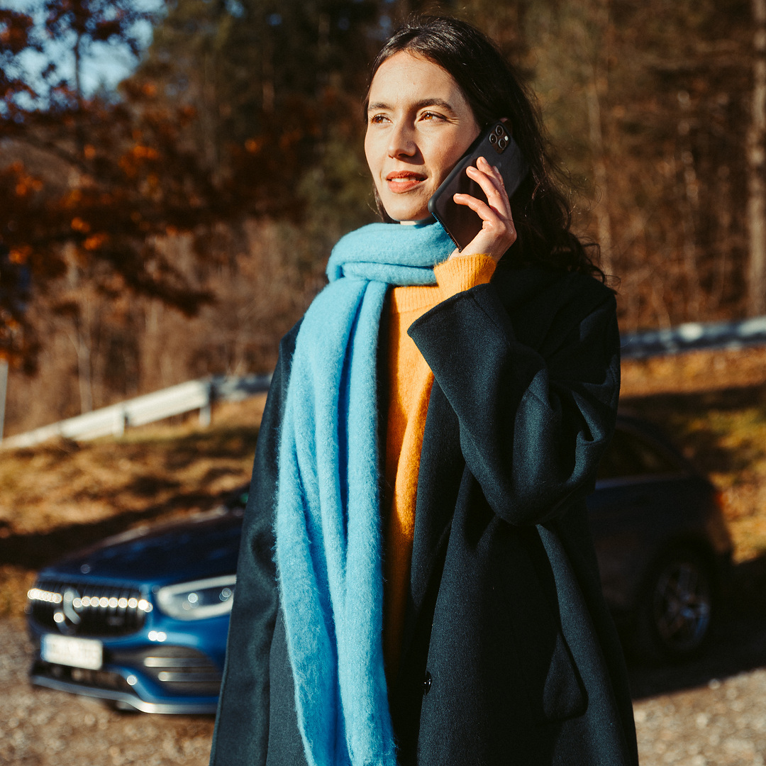 Assistance en cas de panne | Mercedes-Benz Une femme se tient devant son SUV Mercedes et parle au téléphone avec un smartphone.