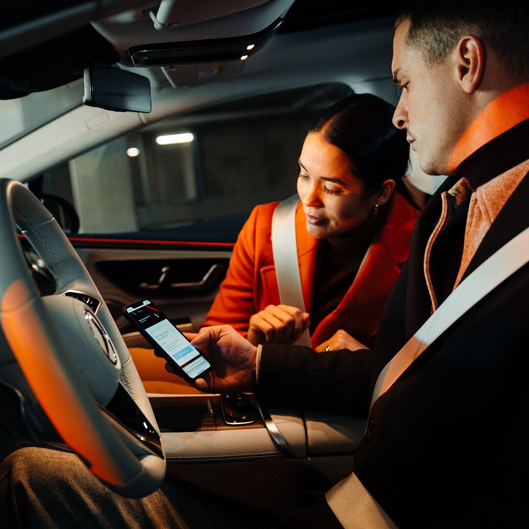 Un couple, assis dans une Mercedes, regarde ensemble un smartphone.