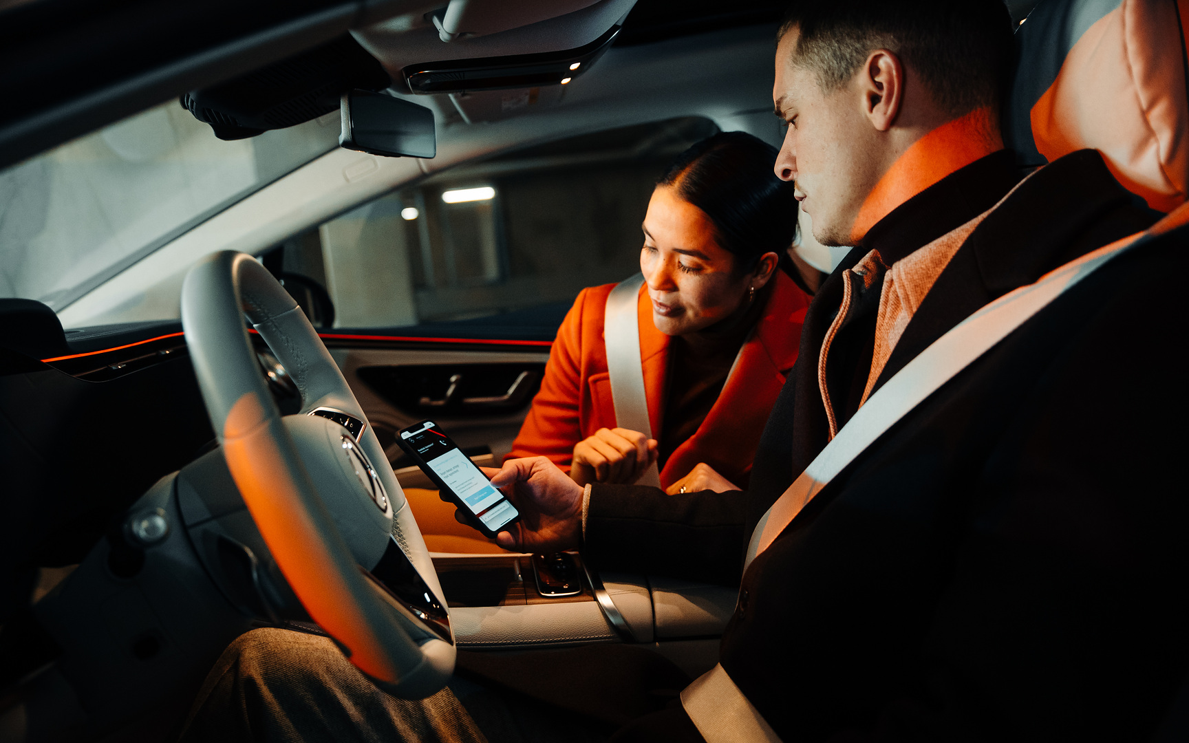 Déclaration de sinistre en ligne | Mercedes-Benz Un couple, assis dans une Mercedes, regarde ensemble un smartphone.