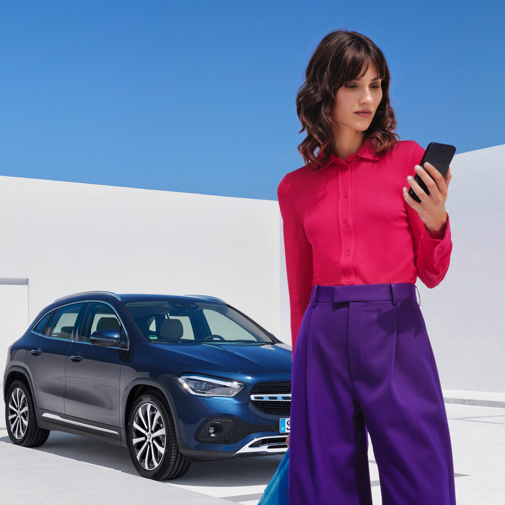 Une femme se tient devant une Mercedes-Benz et consulte son smartphone.
