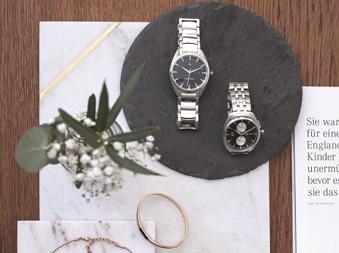 Du haut, le regard est attiré par un vase de muguet, des bijoux et deux montres Mercedes-Benz présentés sur des plaques de marbre.