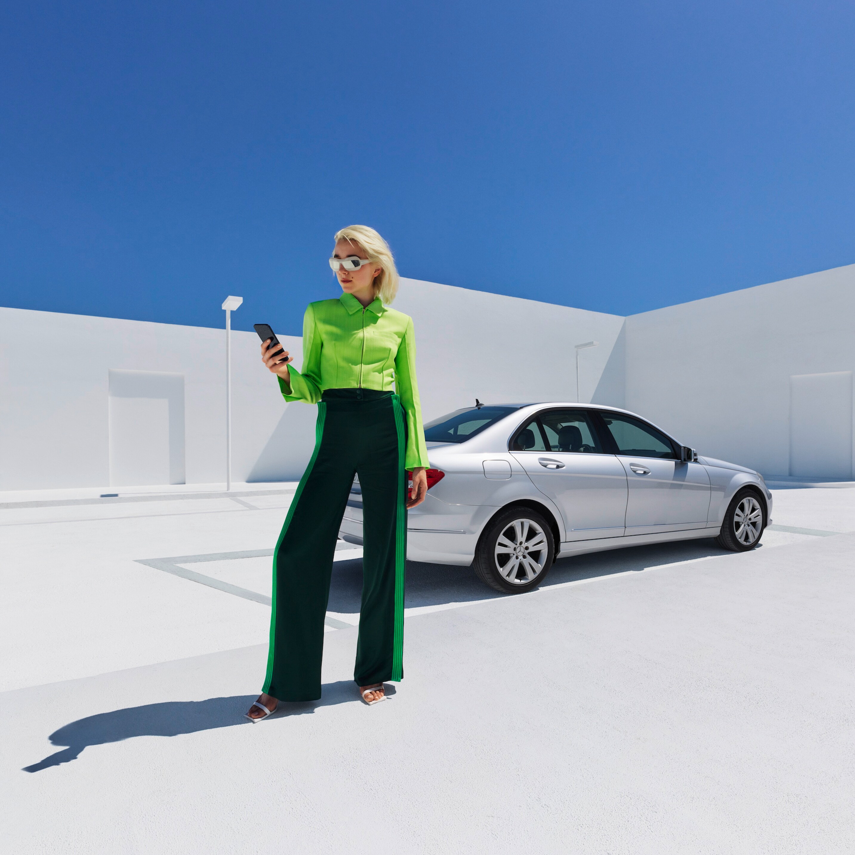 Une femme se tient devant sa Mercedes-Benz et consulte son smartphone.