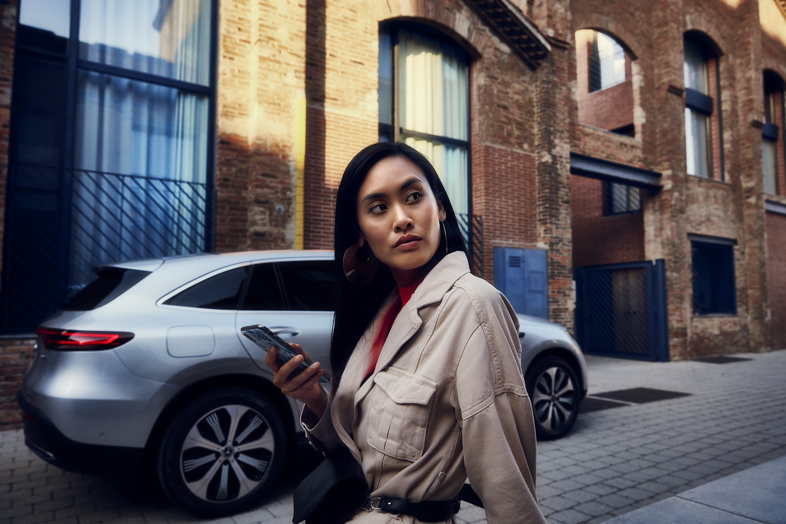 Prise de rendez-vous en ligne | Mercedes-Benz Une femme est debout devant sa Mercedes et tient un smartphone dans sa main droite.