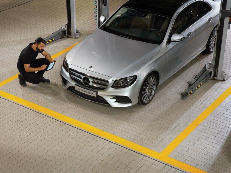 Un technicien Mercedes-Benz est à genoux devant un véhicule et effectue le contrôle technique.