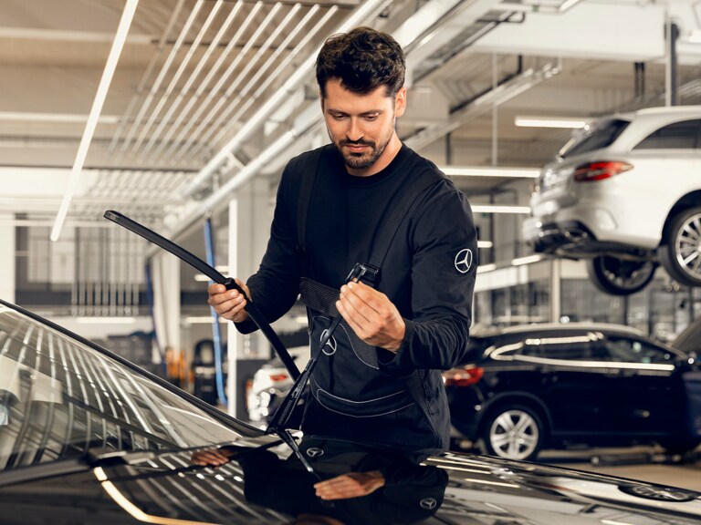 Un technicien Mercedes-Benz est à genoux devant un véhicule et effectue le contrôle technique.