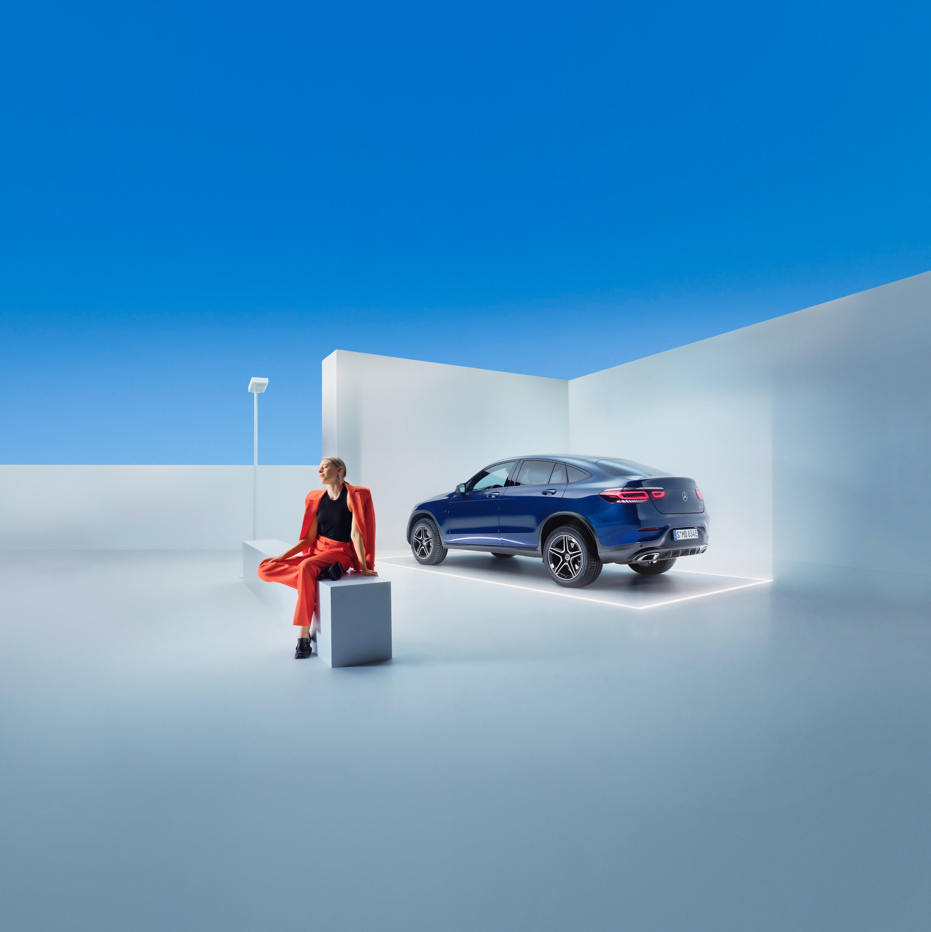 Une femme est assise sur un banc devant une Mercedes-Benz.