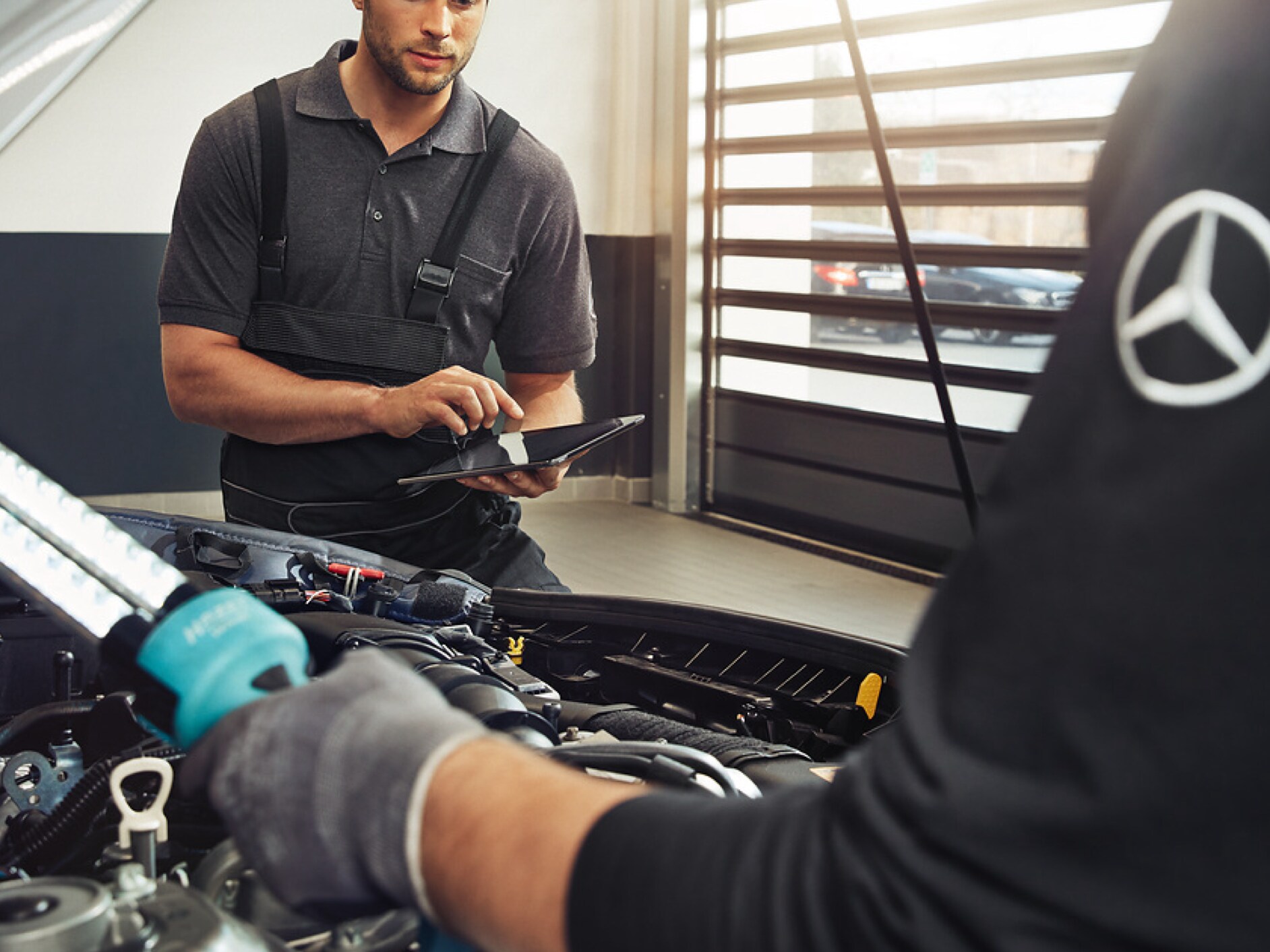 Deux techniciens Mercedes-Benz contrôlent le compartiment moteur d'un véhicule.