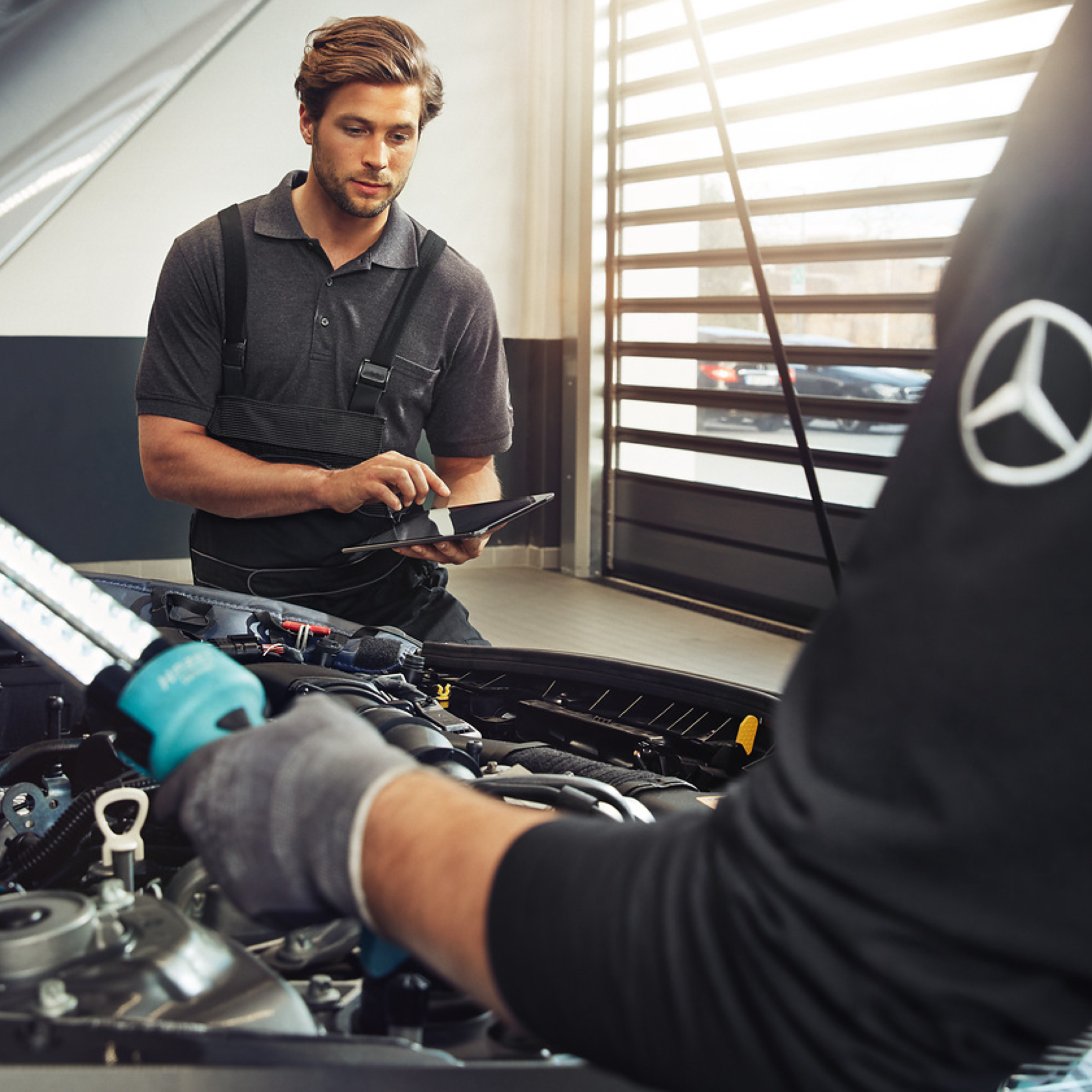 Pièces d'origine Deux techniciens Mercedes-Benz contrôlent le compartiment moteur d'un véhicule.