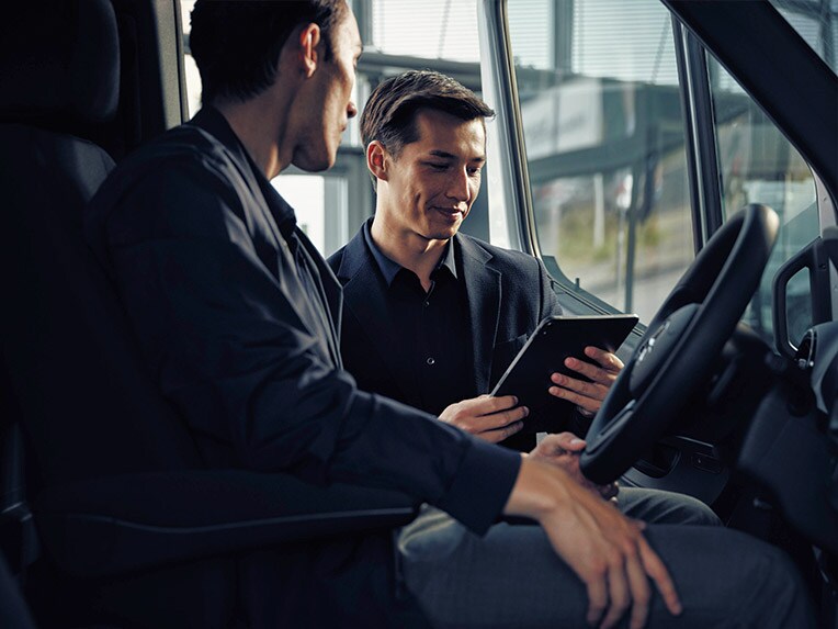 Deux personnes assises à l'avant d'un utilitaire Mercedes-Benz consultent une tablette numérique en concession.