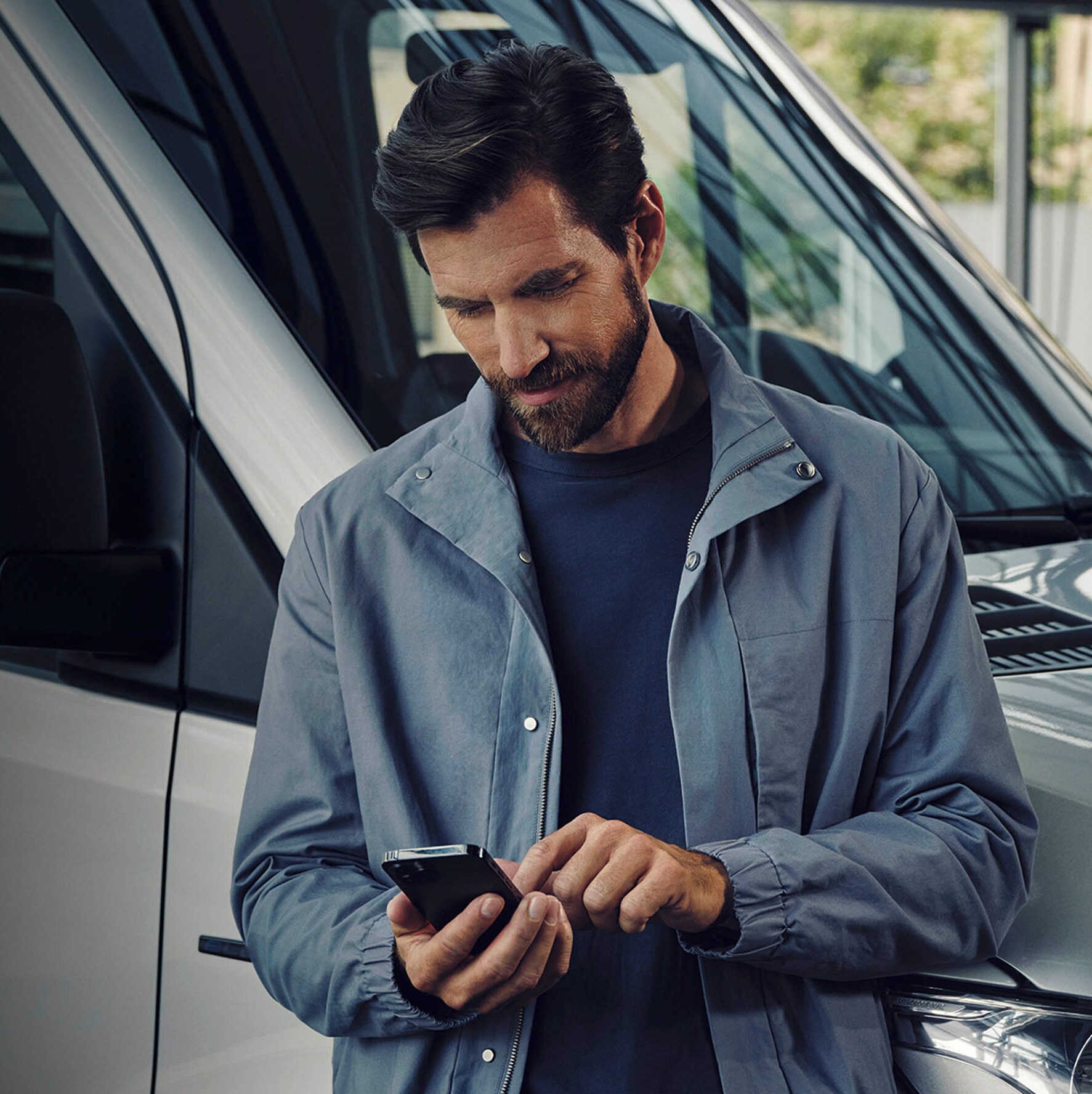 Un homme regarde un téléphone portable à côté d'un Mercedes-Benz eSprinter