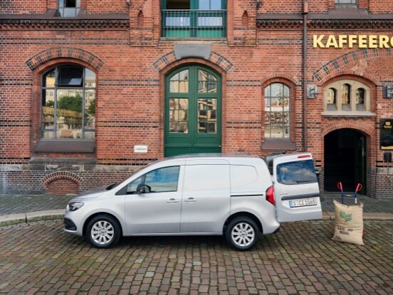 Un Citan fourgon de Mercedes-Benz devant un bâtiment en briques, avec la porte arrière ouverte.