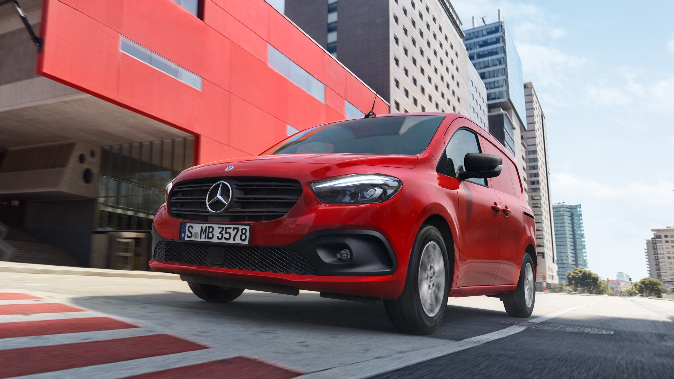 Mercedes-Benz GLA rouge roulant en milieu urbain devant un bâtiment moderne.
