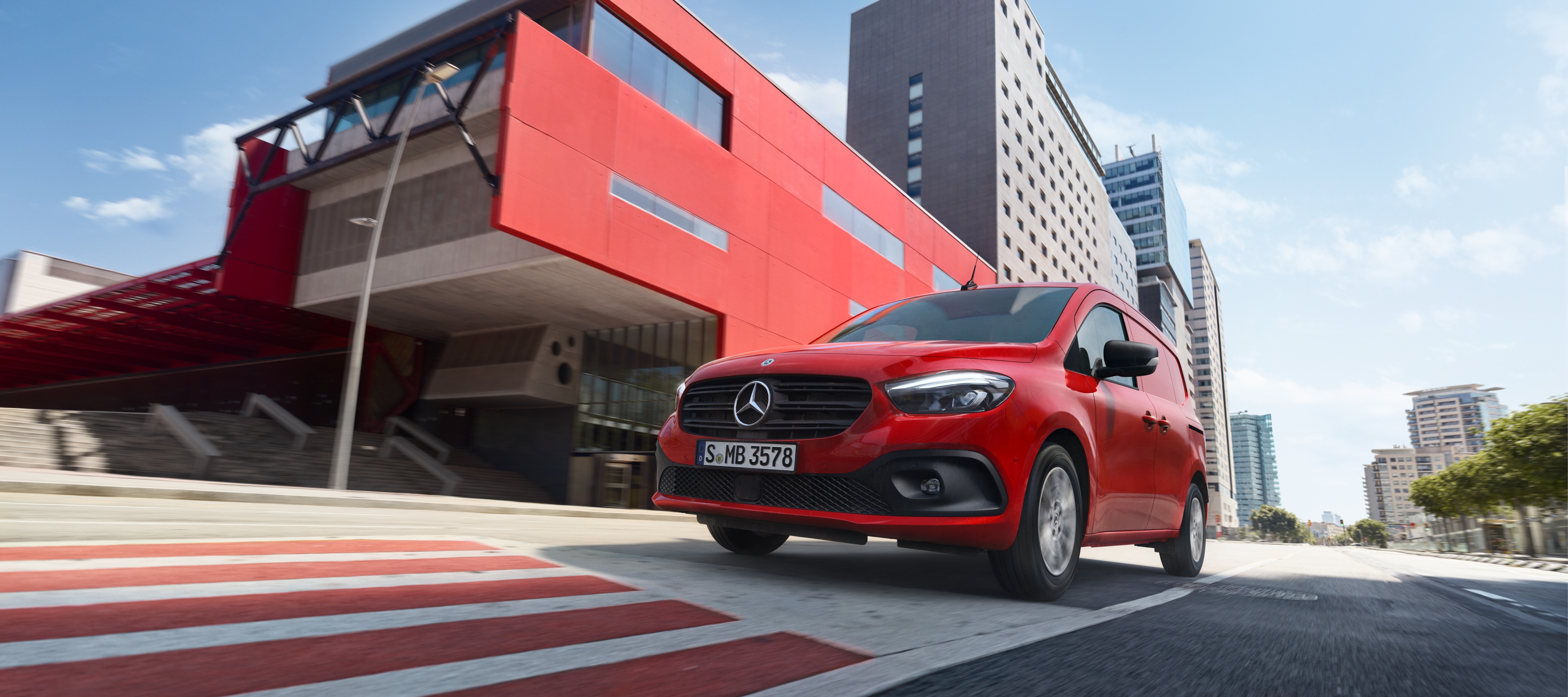 Citan Gebrauchtwagen von Mercedes-Benz Mercedes-Benz GLA rouge roulant en milieu urbain devant un bâtiment moderne.