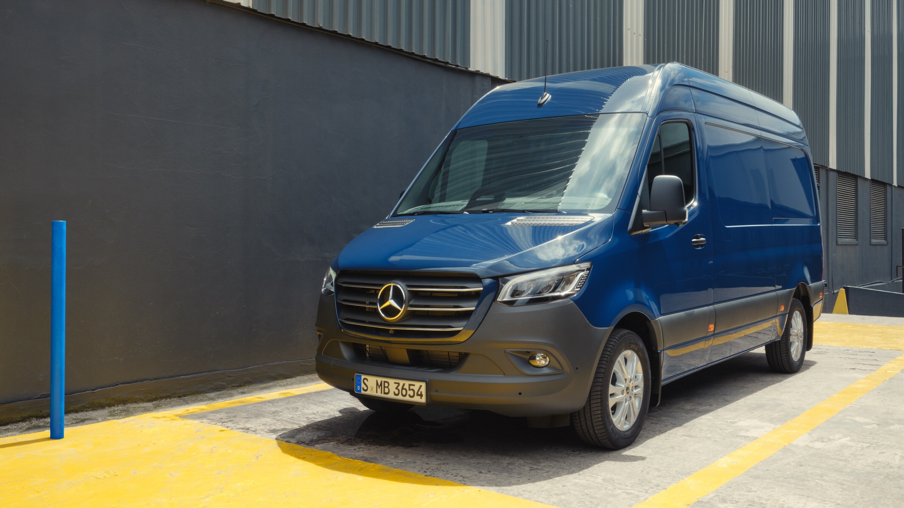 Mercedes-Benz Sprinter bleu stationné sur une place de parking devant un bâtiment industriel.