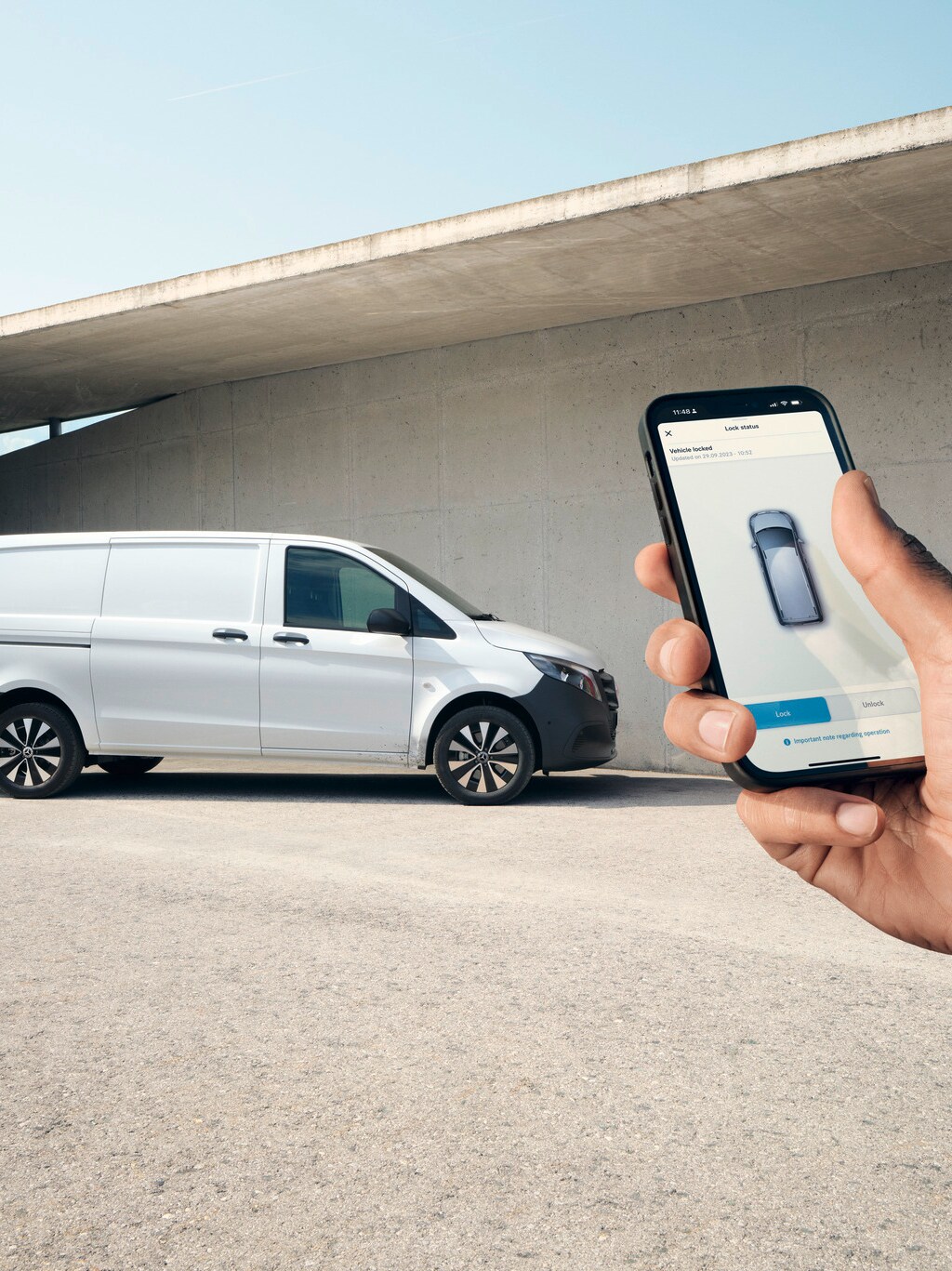 Main tenant un smartphone montrant l'application Mercedes me. Vito fourgon en arrière-plan.