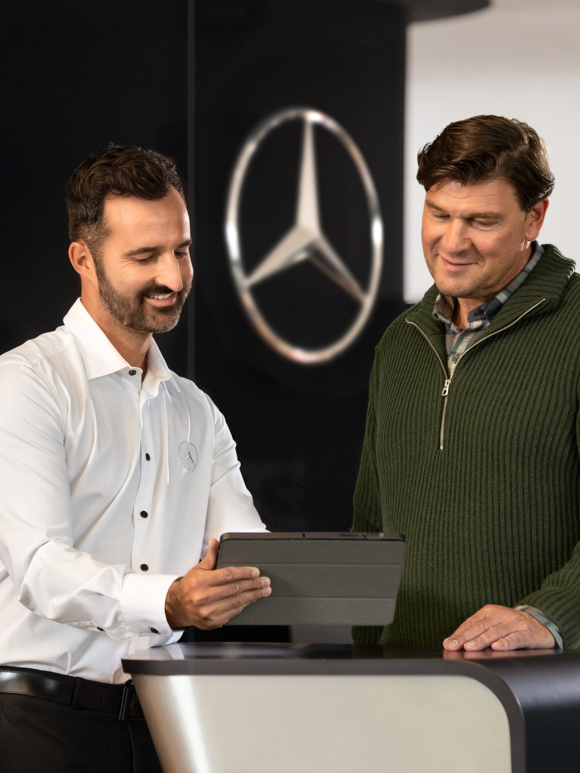 Un employé de Mercedes conseille les clients au comptoir à l'aide d'une tablette - assistance individuelle et conseils commerciaux dans la concession.