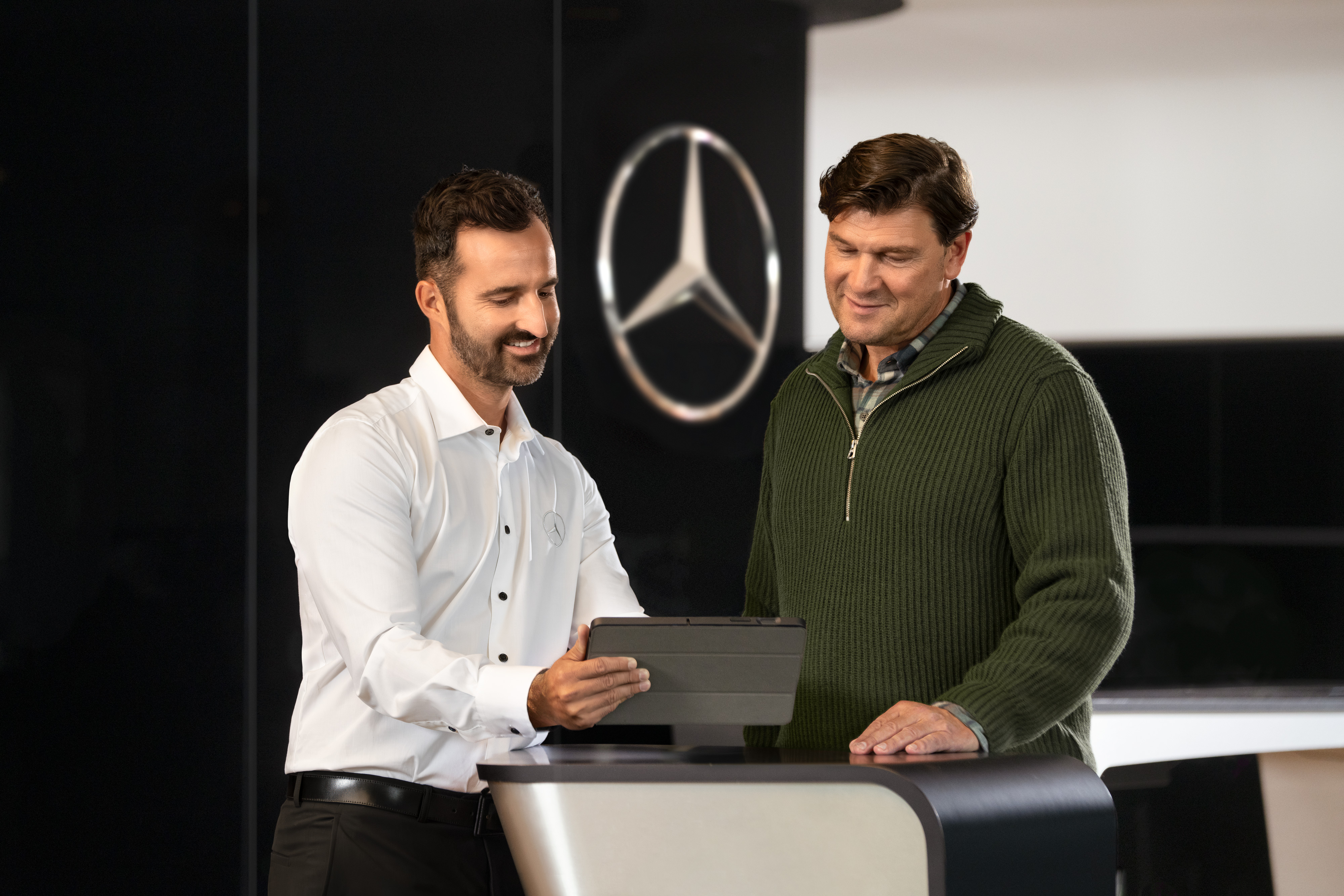 Mercedes-Benz | Assistance pour utilitaires légers | Soutien individuel Un employé de Mercedes conseille les clients au comptoir à l'aide d'une tablette - assistance individuelle et conseils commerciaux dans la concession.