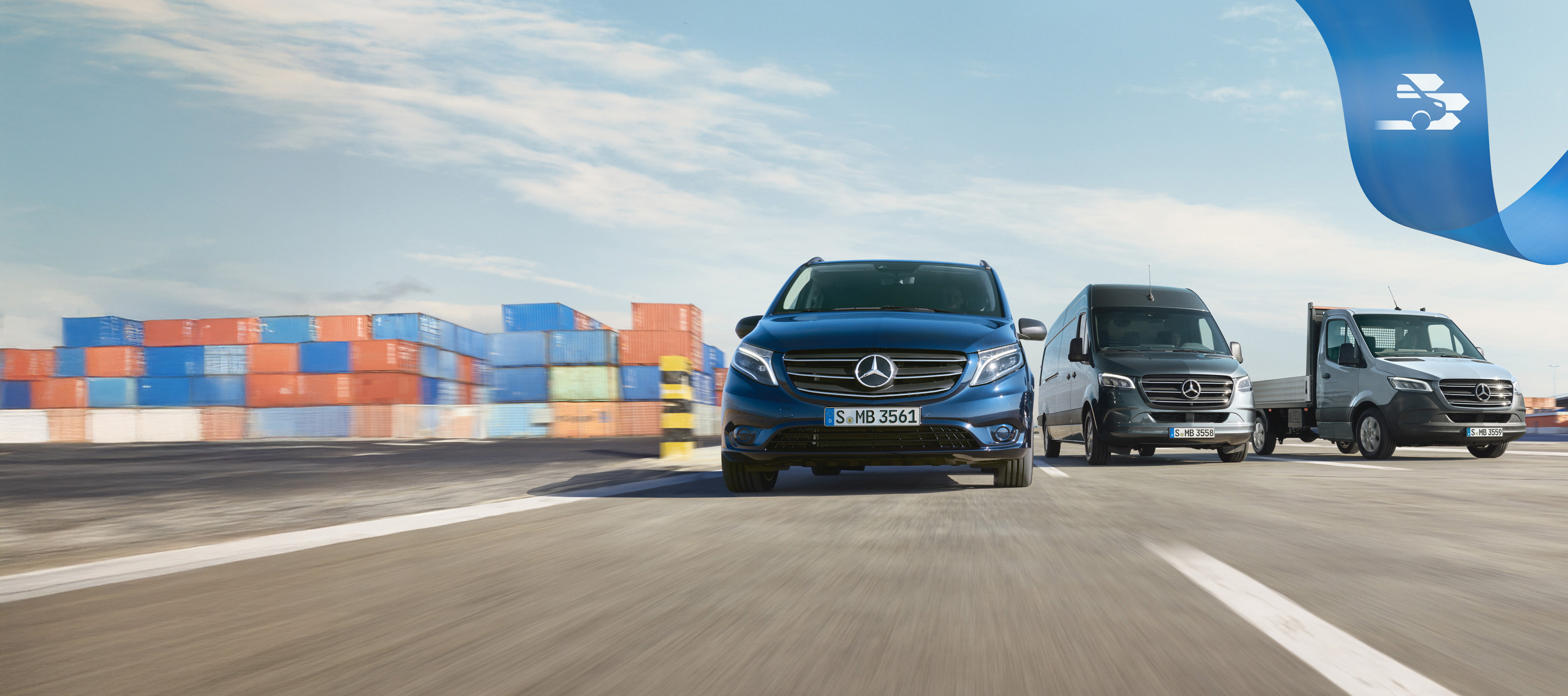 Mercedes Benz | Confort Mobilovan Une série d’utilitaires légers Mercedes-Benz sur la route avec des conteneurs d'expédition en l'arrière-plan.