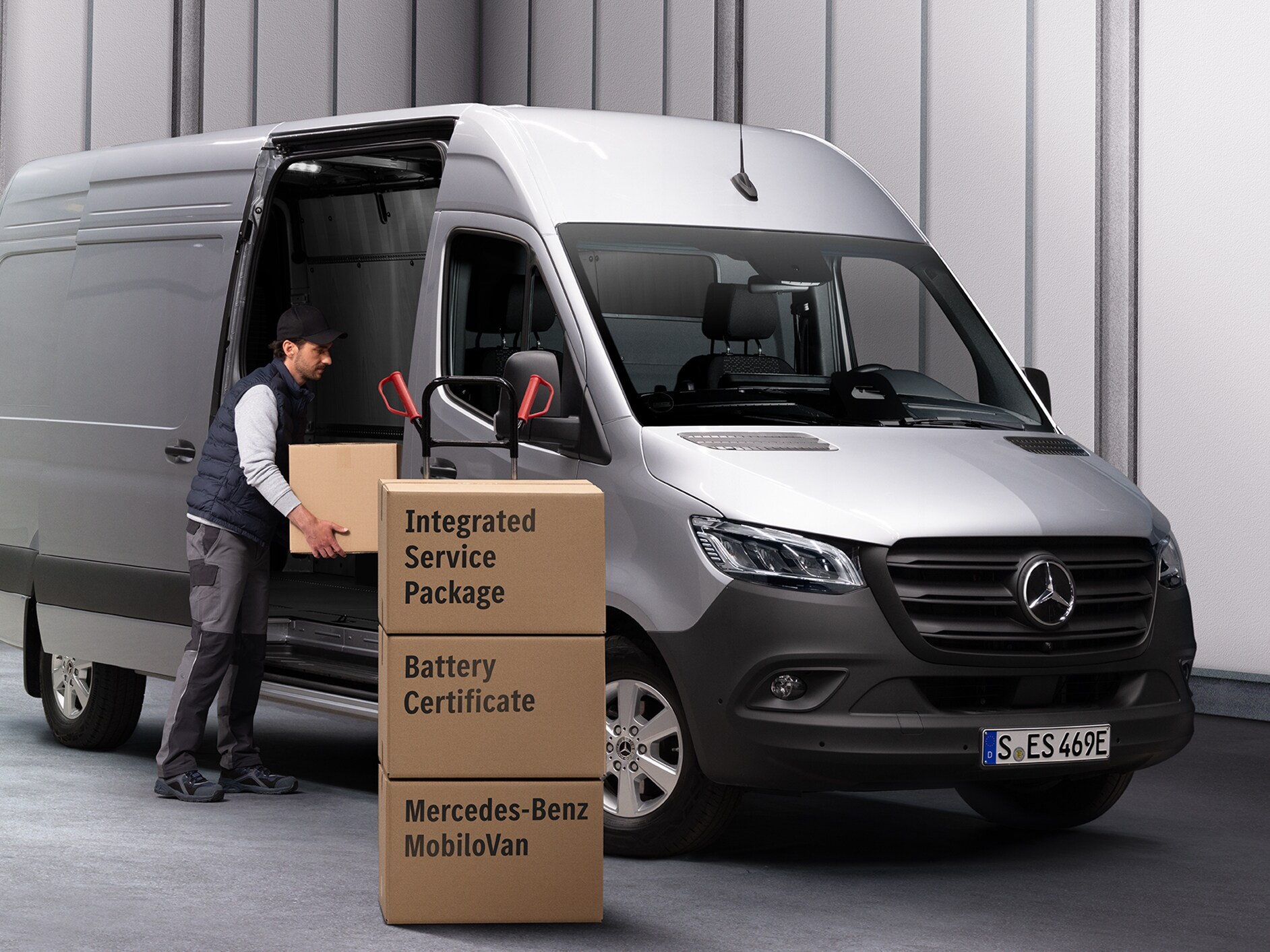 Une personne déchargeant des cartons d'une Mercedes-Benz eSprinter. Trois boîtes sont empilées devant l'utilitaire léger. Les boîtes sont étiquetées avec les noms des produits de Mercedes-Benz Service.