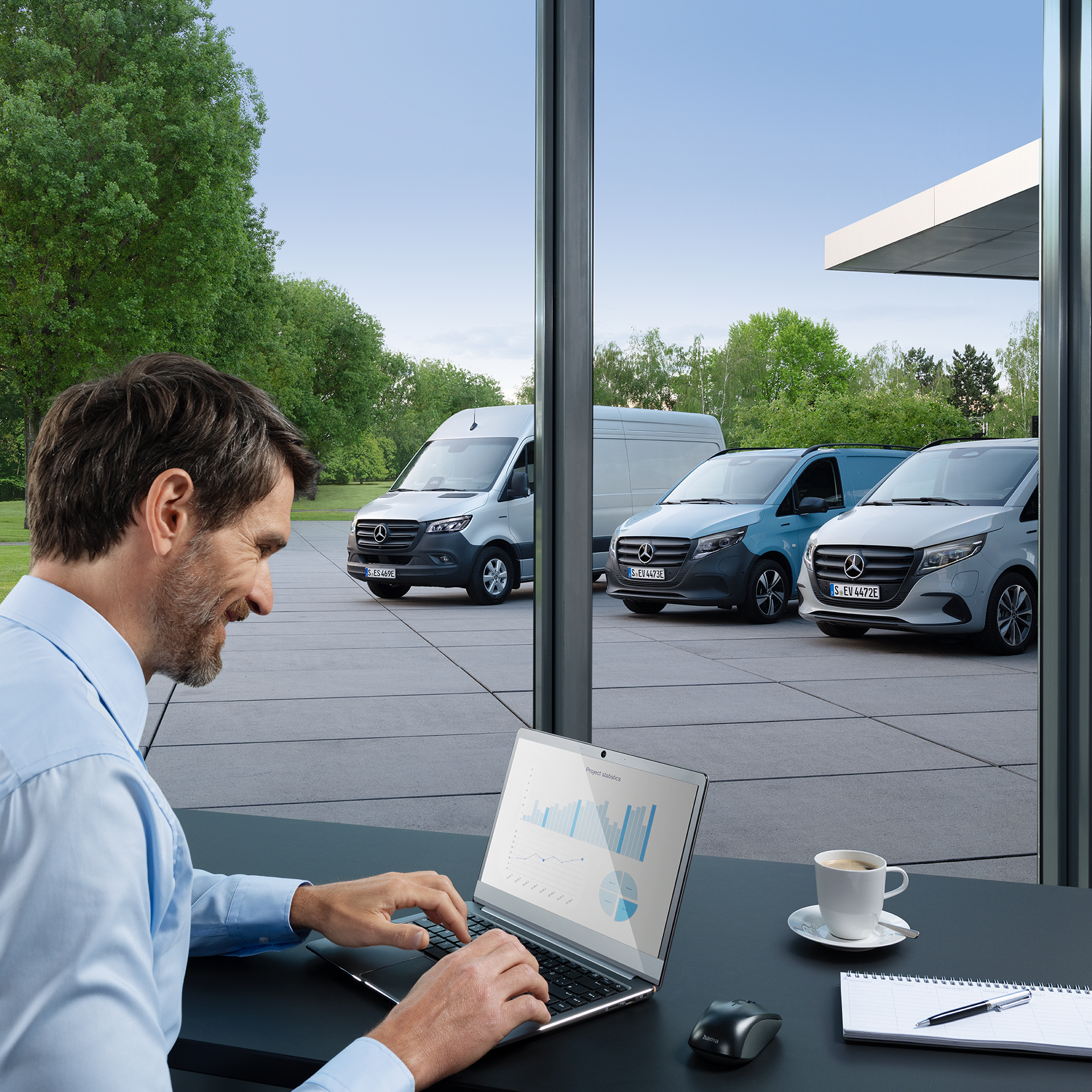 Véhicules électriques Mercedes-Benz | Mercedes-Benz ServiceCare Une personne assise devant un ordinateur portable dans un bureau. Trois utilitaires légers électriques Mercedes-Benz sont garés à l'extérieur.