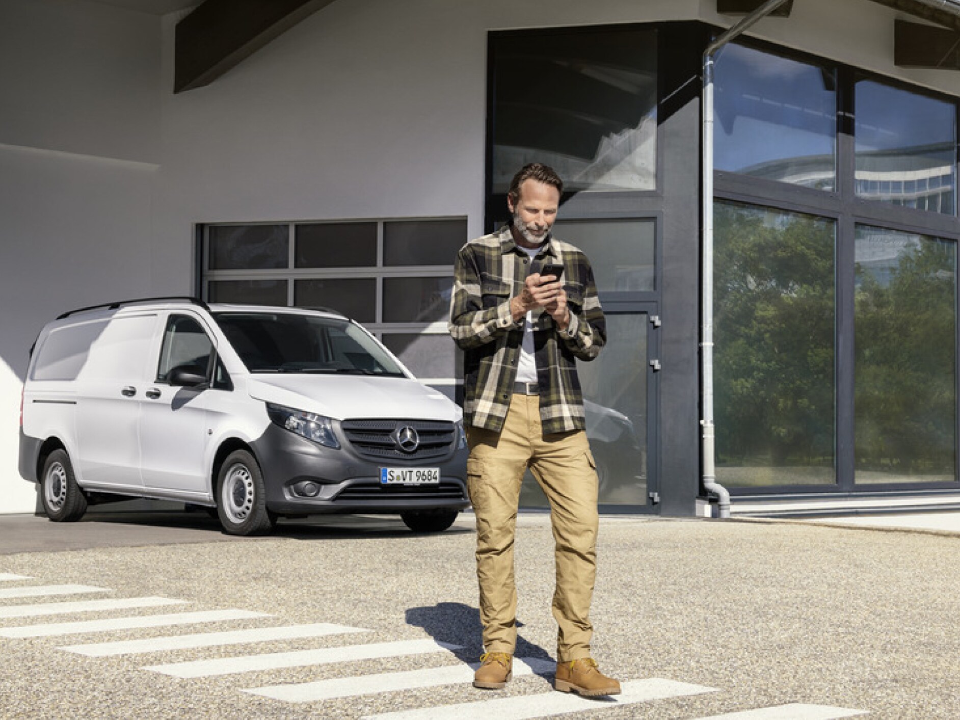 Une personne avec un smartphone devant un Mercedes-Benz Vito.
