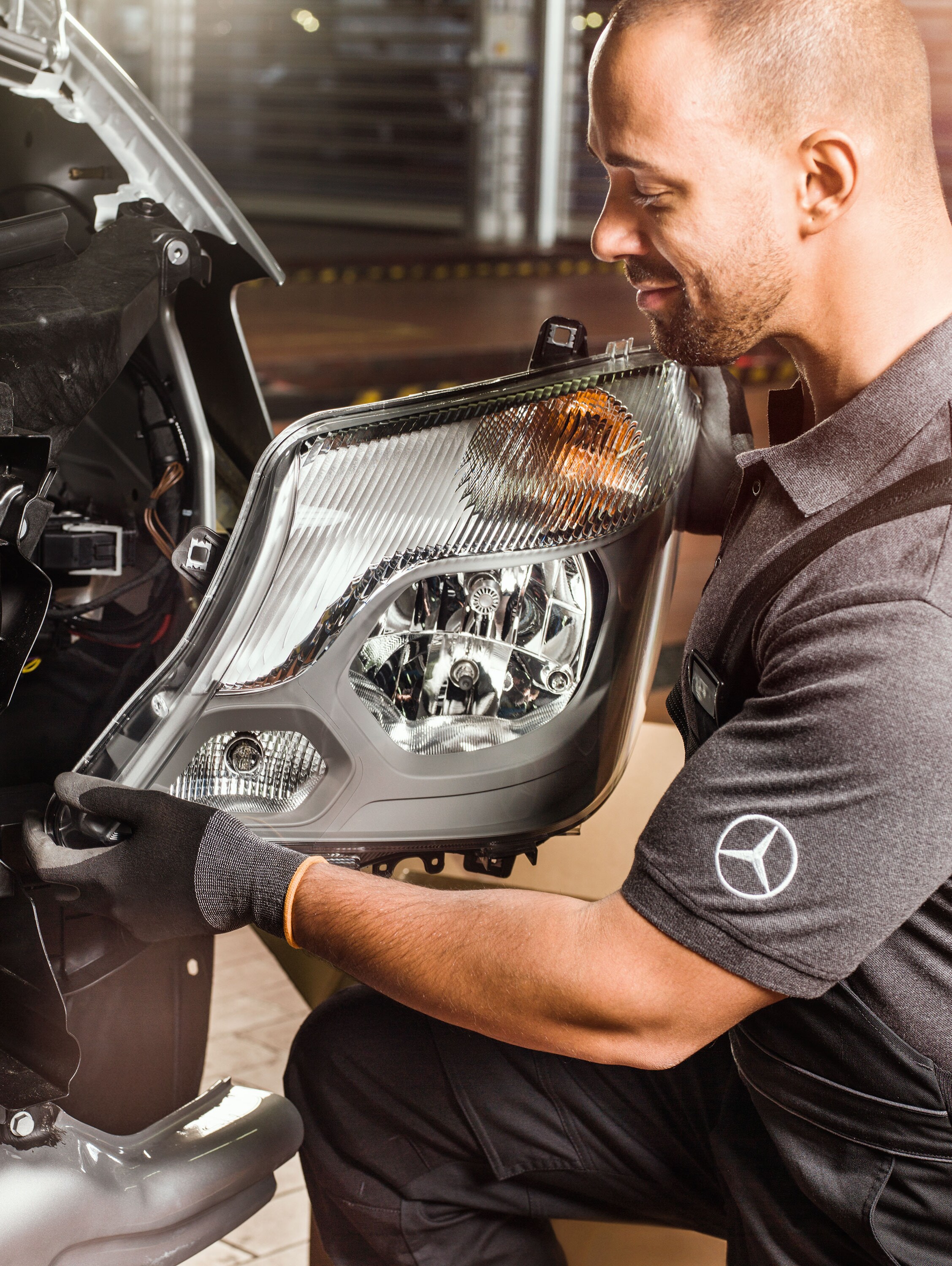 Mécanicien vérifiant les pièces d'origine Mercedes-Benz devant un moteur de Sprinter ouvert, correspondant au catalogue de pièces détachées Mercedes.