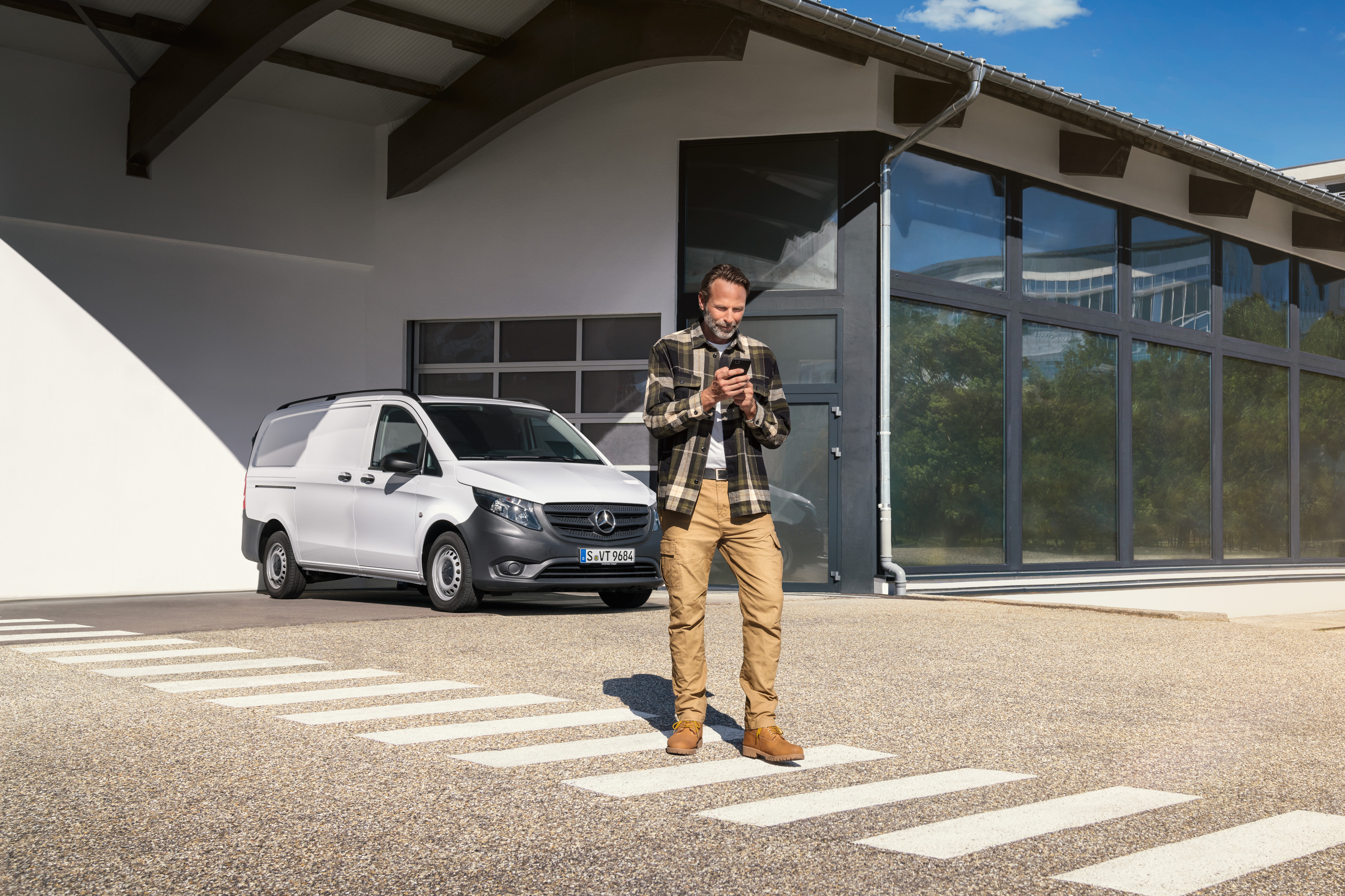 Mercedes-Benz | Service pour véhicules électriques | Support numérique Un homme se tient devant un utilitaire léger Mercedes-Benz Vito, utilisant son smartphone.