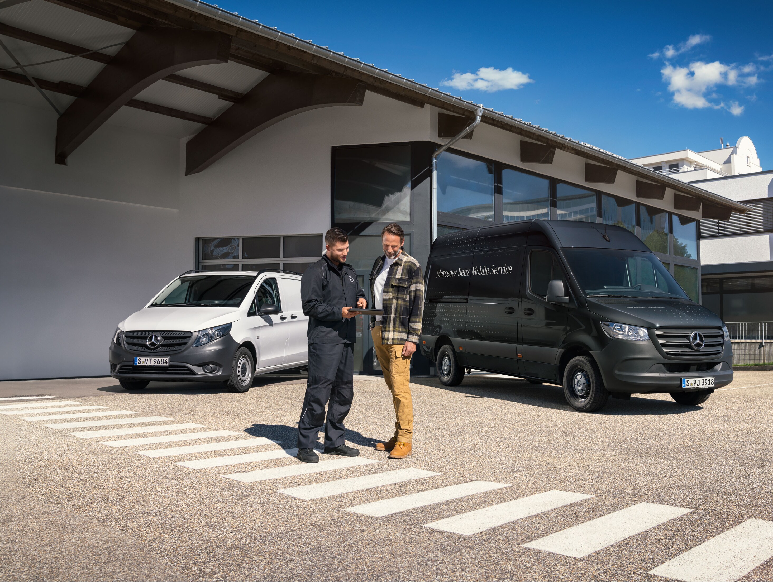 Two men talking in front of a white Mercedes-Benz Vito van and black Mercedes-Benz Sprinter van.