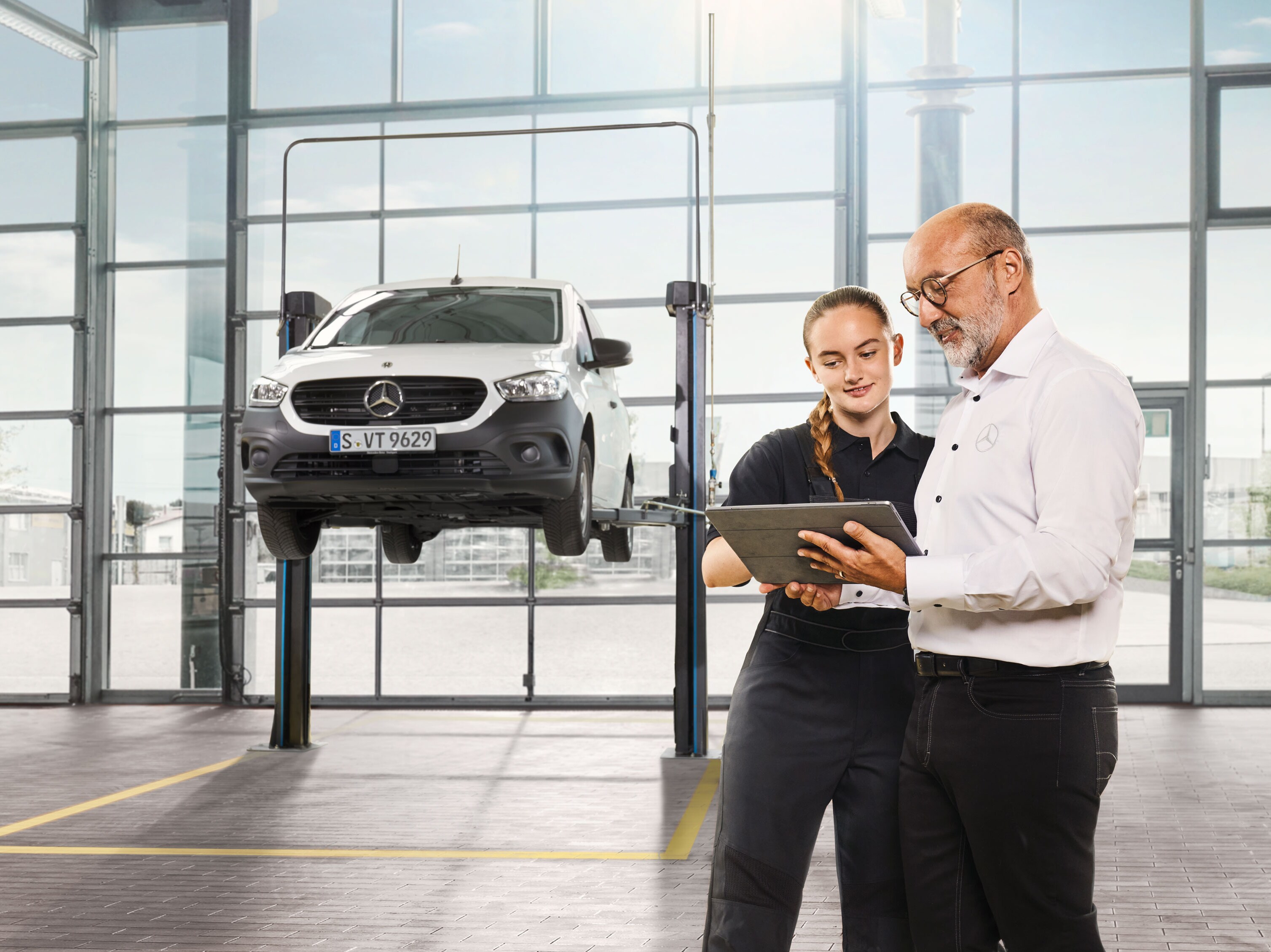 Two employees discuss the commercial vehicle service on a jacked-up Mercedes-Benz van in the workshop.