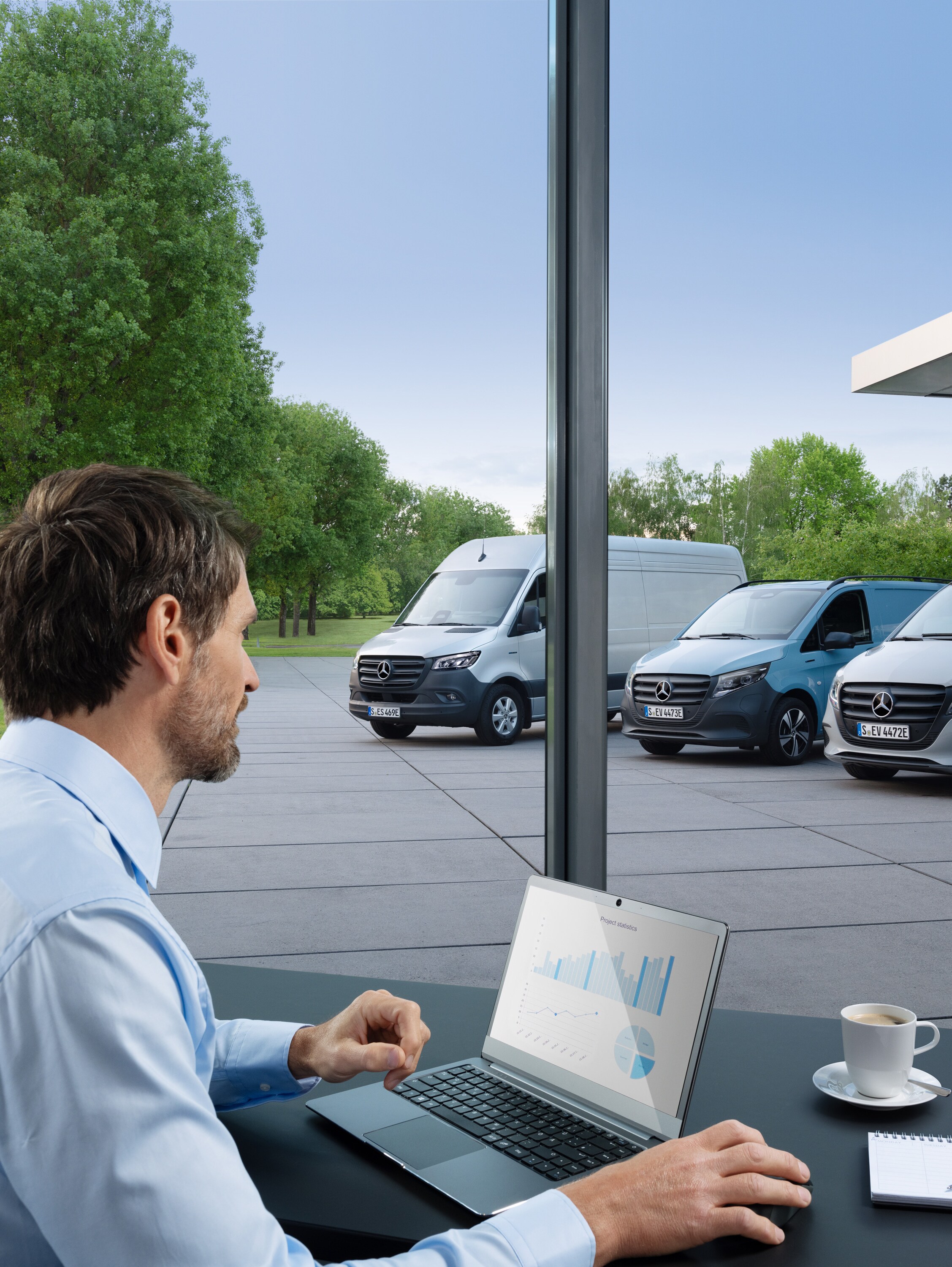 Un homme surveille plusieurs utilitaires légers Mercedes-Benz stationnées à l'aide d'un ordinateur portable, symbole de la gestion numérique de la flotte.